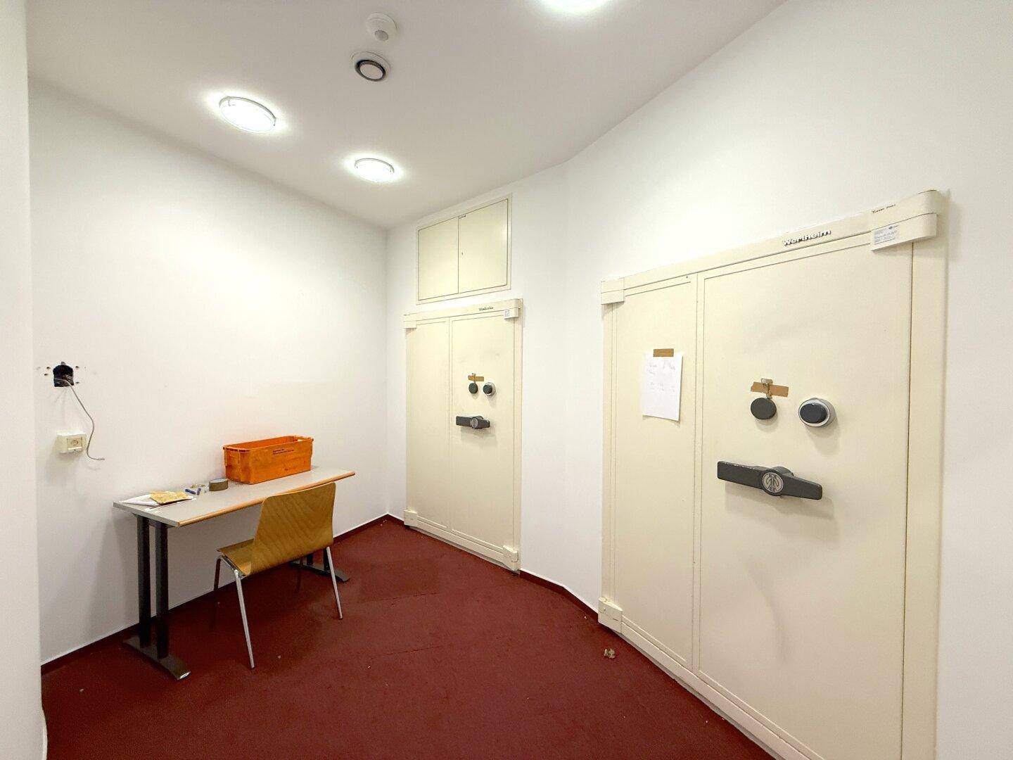 Sicherheitsraum mit zwei großen Tresoren, einem kleinen Schreibtisch und rotem Teppichboden.