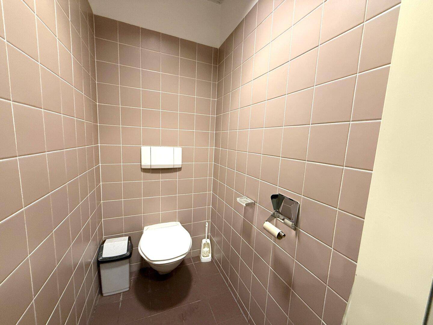 Toilettenkabine mit wandhängendem WC und durchgehend gefliesten Wänden in hellem Braunton.