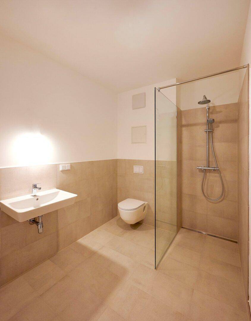 Modernes Badezimmer mit ebenerdiger Dusche, Wand-WC und hellem Fliesenboden.
