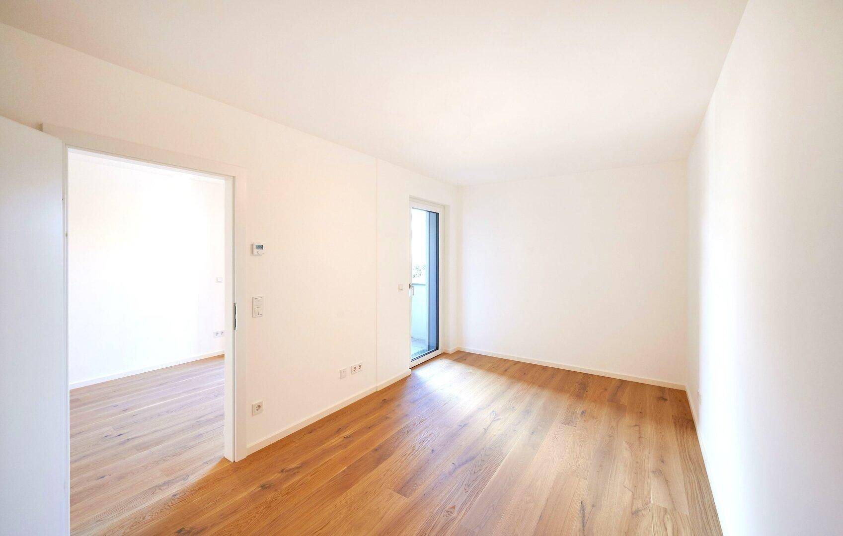 Helles, leeres Schlafzimmer mit Parkettboden und direktem Zugang zu einem Balkon.