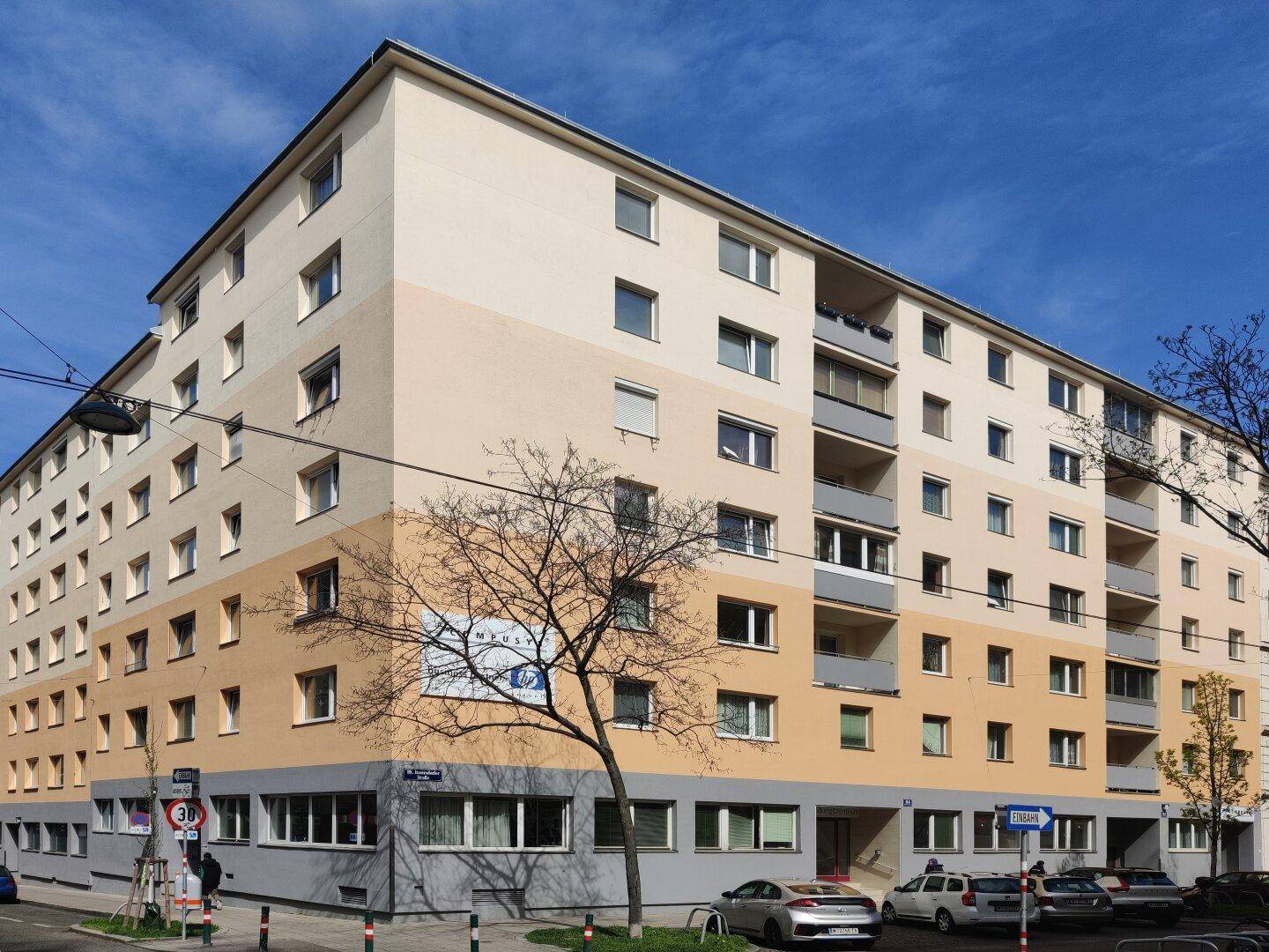 Mehrstöckiges Wohn- und Geschäftsgebäude mit gestufter Fassade und vielen Fenstern an einem sonnigen Tag.