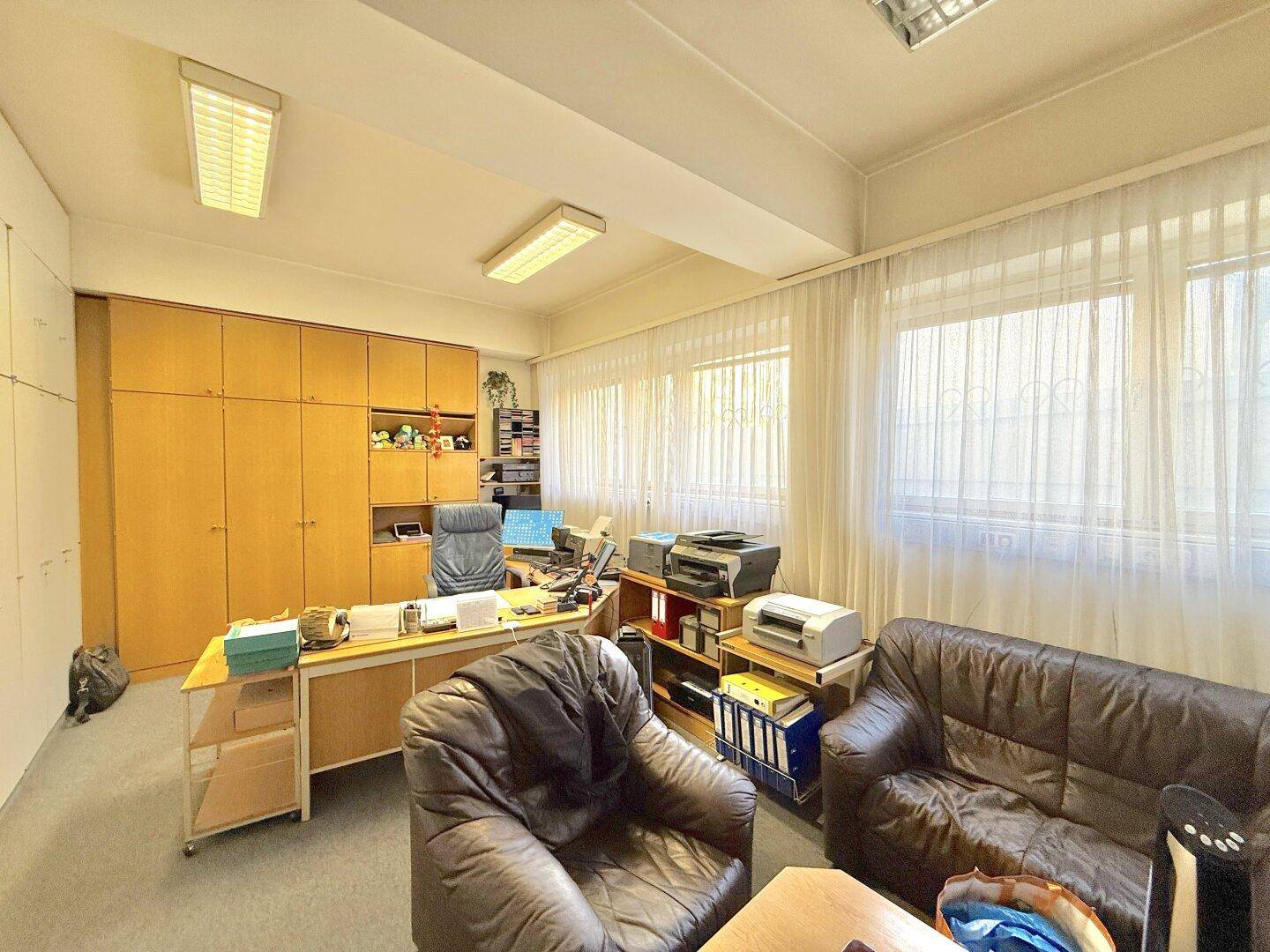 Büro mit großem Schreibtisch, Ledersofa und -sessel, sowie viel Stauraum in den Schränken.