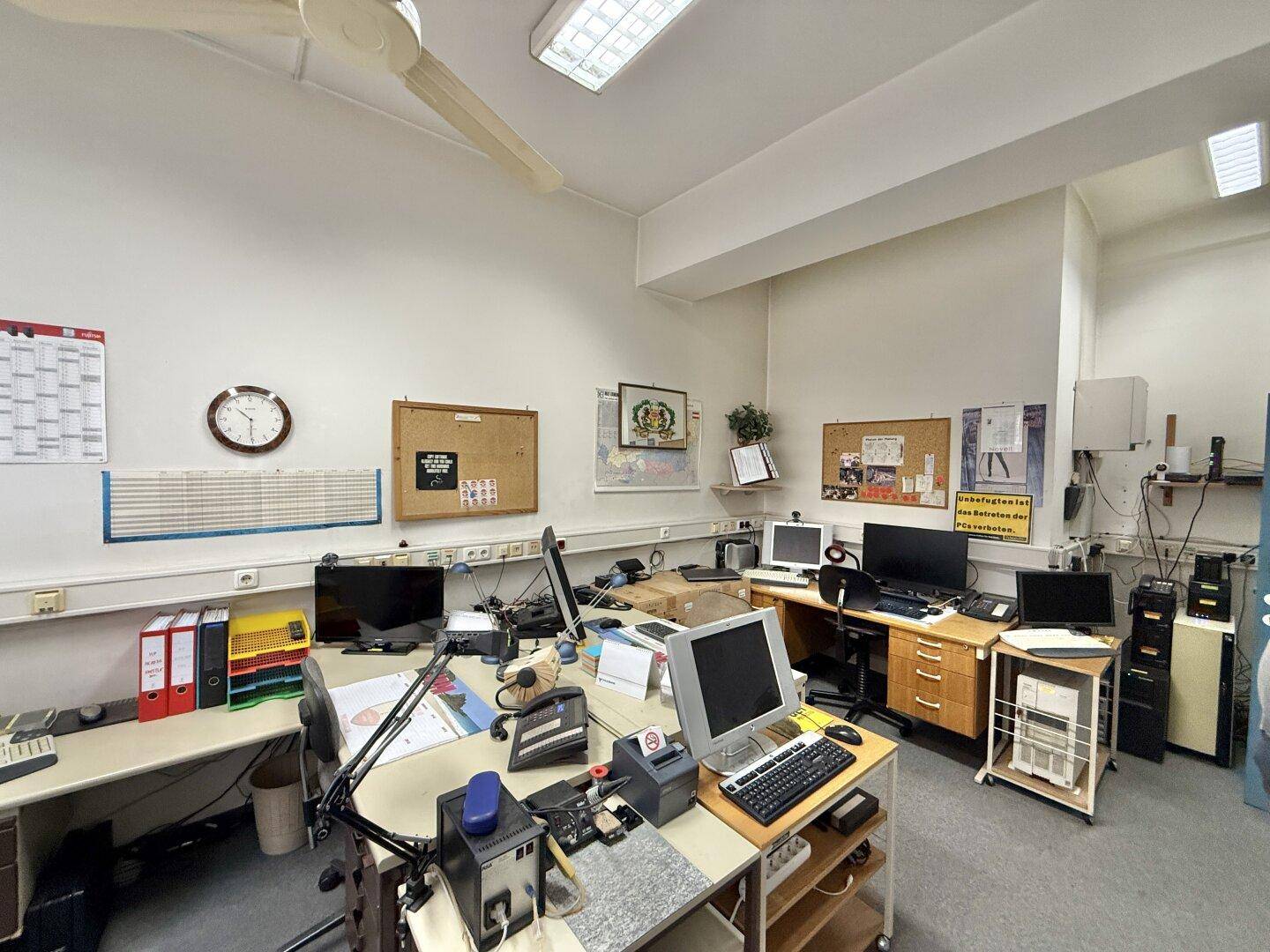 Detailansicht eines Bürobereichs mit mehreren Computern, Pinnwänden und funktionaler Einrichtung.