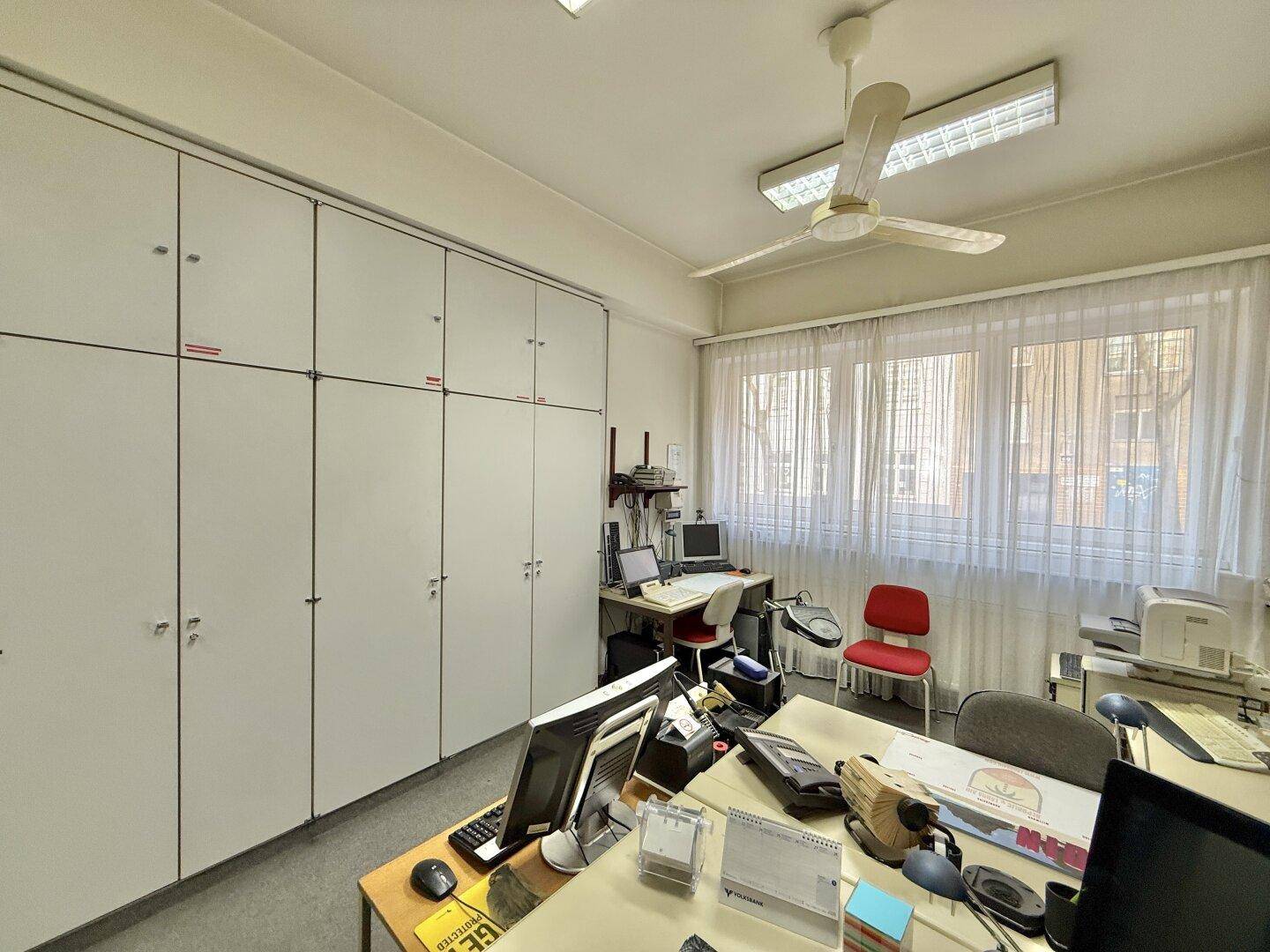 Büro mit weißen Aktenschränken, mehreren Arbeitsplätzen und einem Deckenventilator für Komfort.