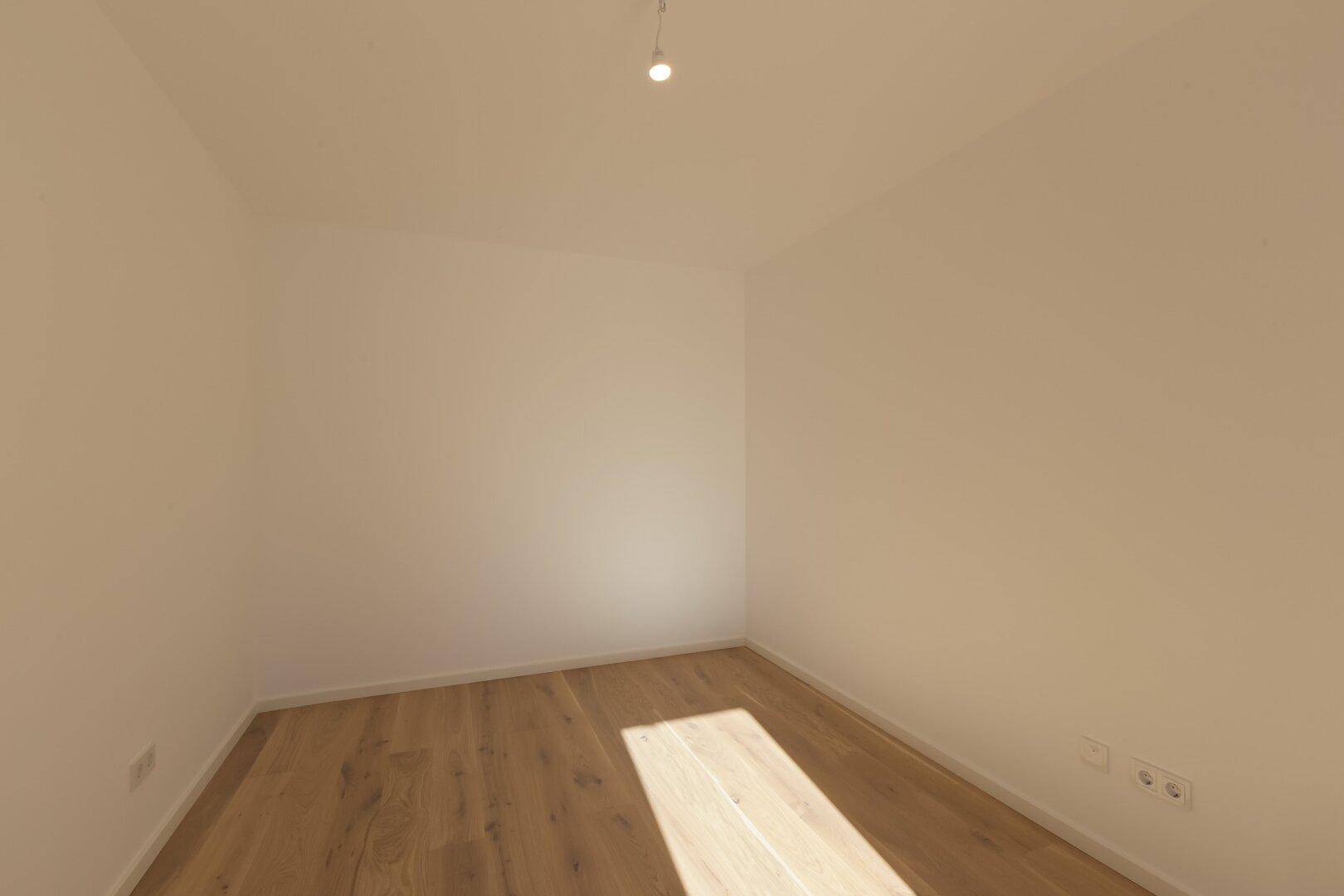 Leeres Zimmer mit Holzboden und weißen Wänden, ideal als Kinder- oder Arbeitszimmer.