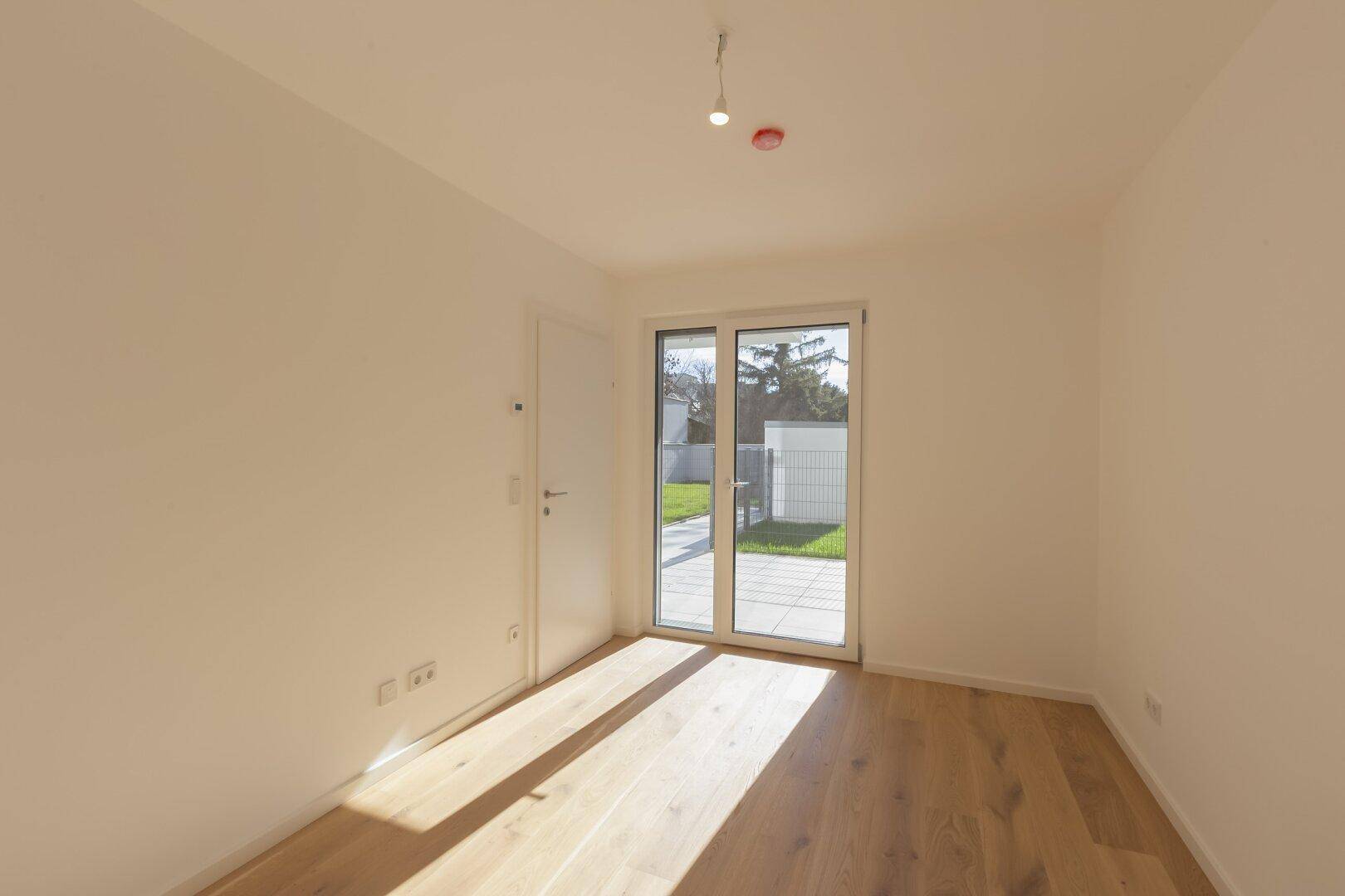 Helles Schlafzimmer mit Holzboden und großem Fenster, das Zugang zum Außenbereich bietet.