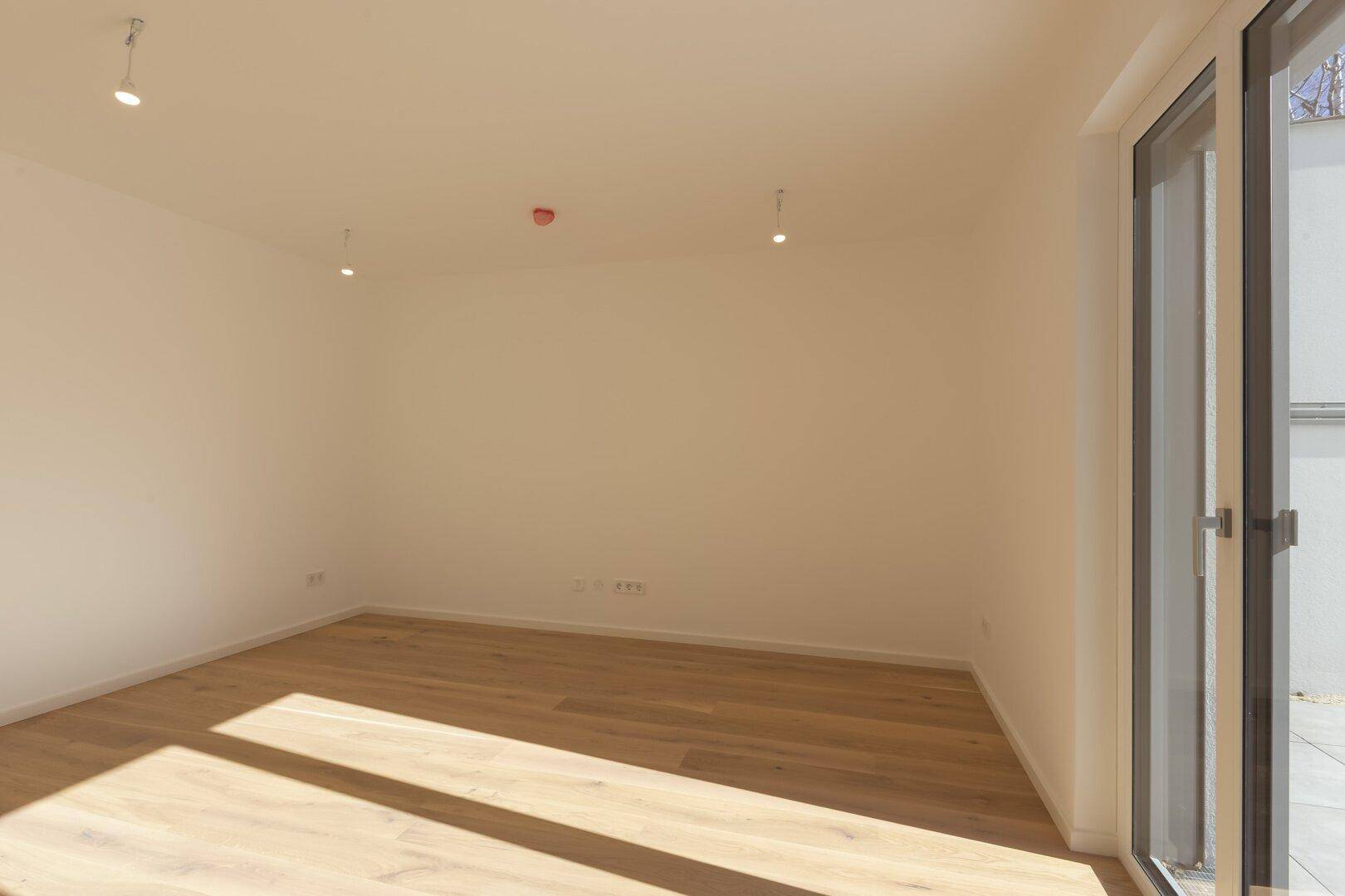 Helles Zimmer mit Holzboden und großem Fenster, das viel Sonnenlicht hereinlässt.