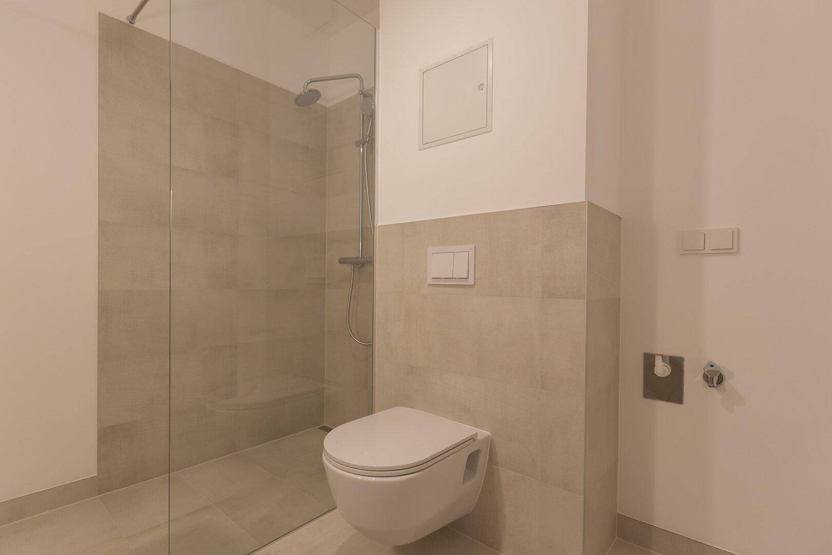 Modernes Badezimmer mit wandhängendem WC, begehbarer Dusche und beigefarbenen Fliesen.
