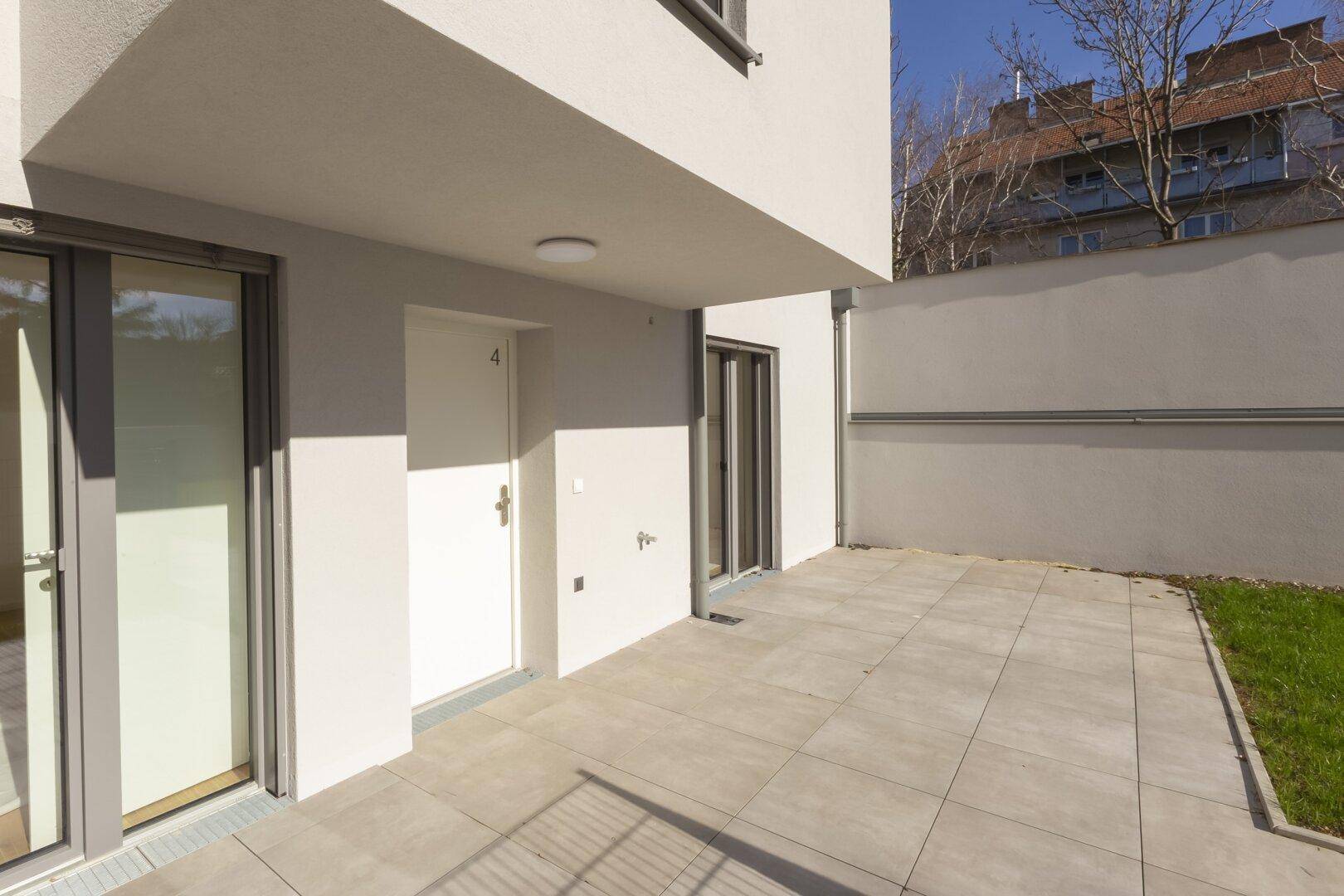 Helle Terrasse im Erdgeschoss mit Zugang zu den Innenräumen und moderner Fassade.