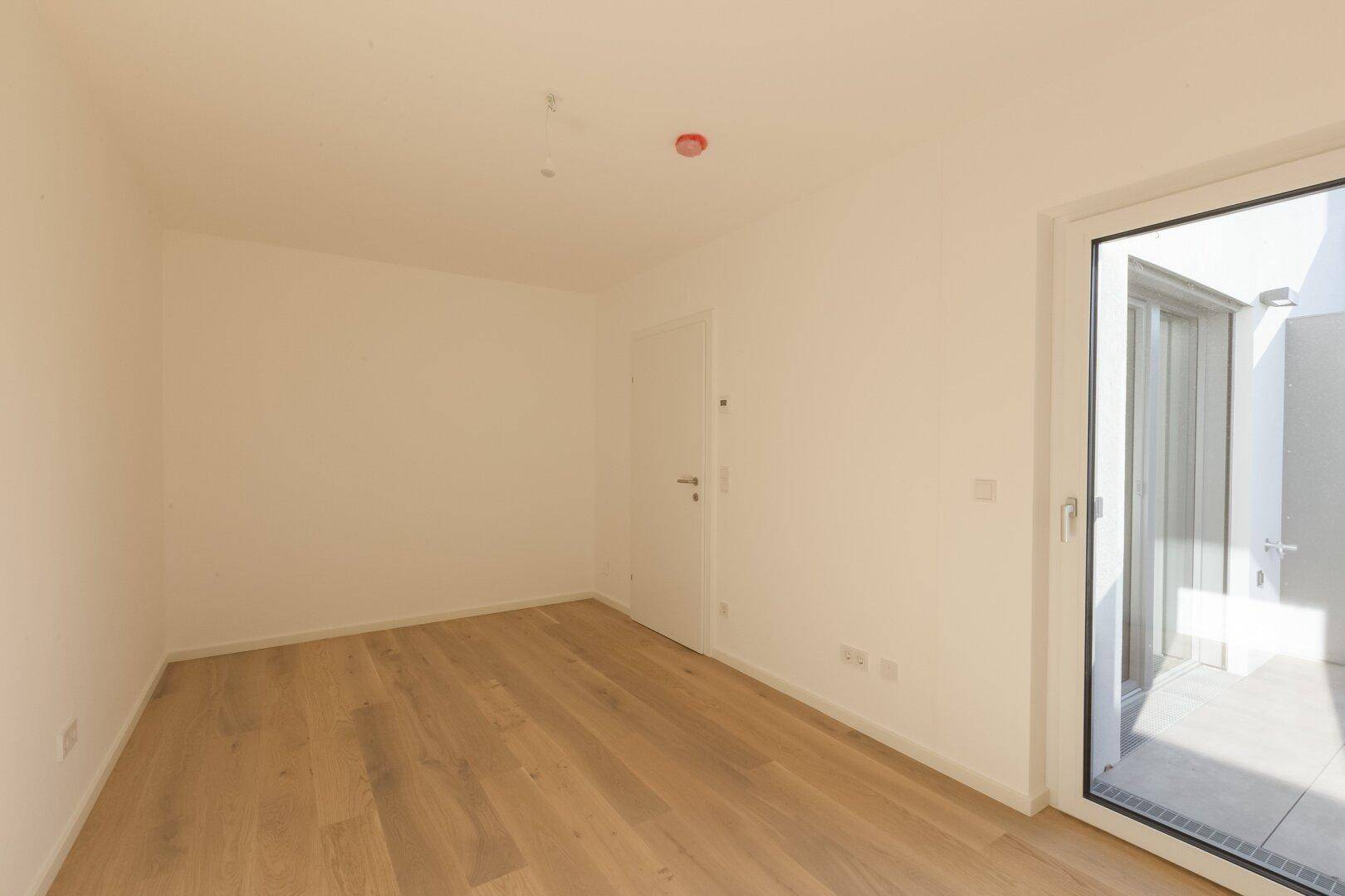 Geräumiges Zimmer mit Holzboden und Zugang zu einem Außenbereich, ideal als Schlafzimmer.