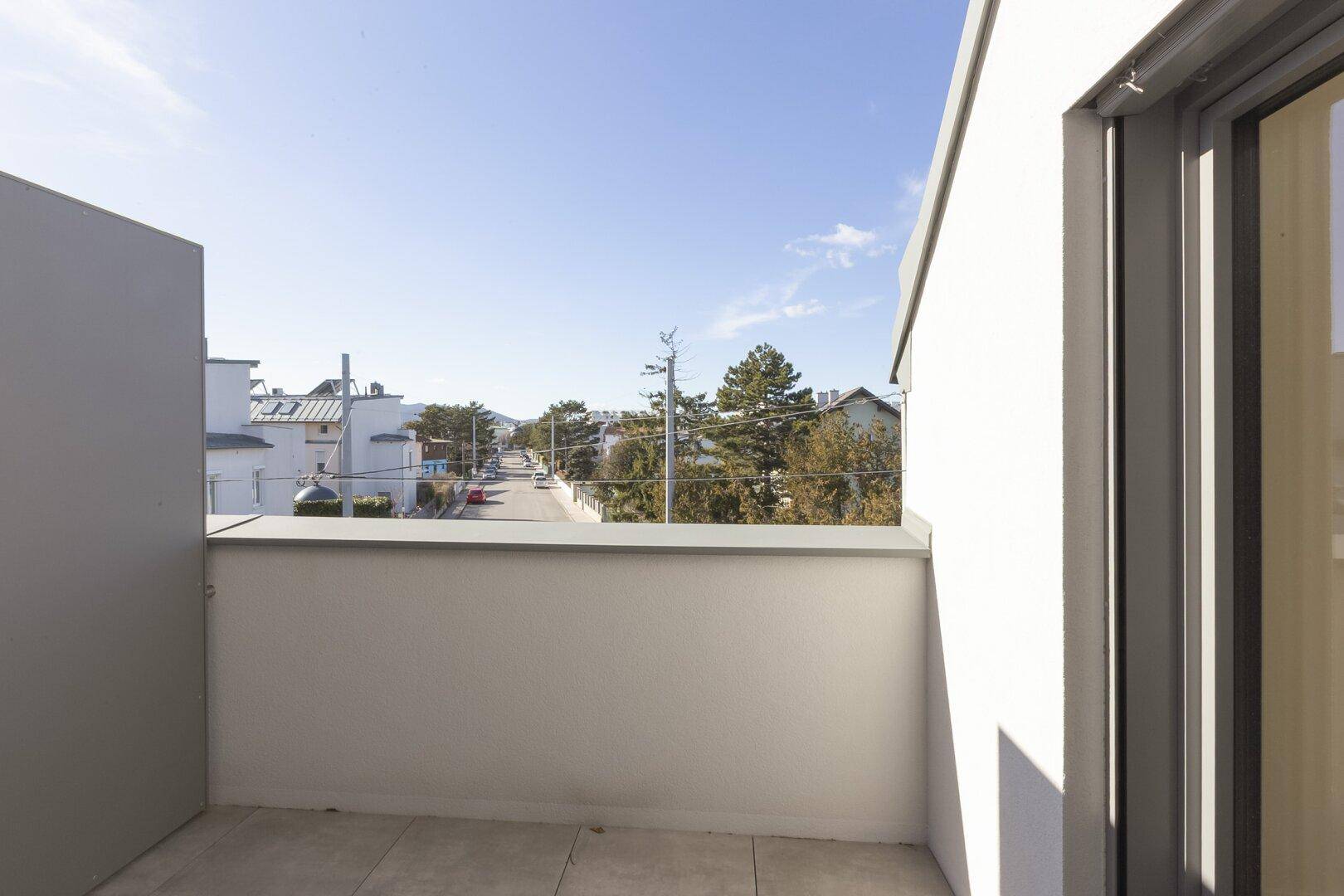 Sonniger Balkon mit Ausblick auf die ruhige Wohnstraße und grüne Umgebung.