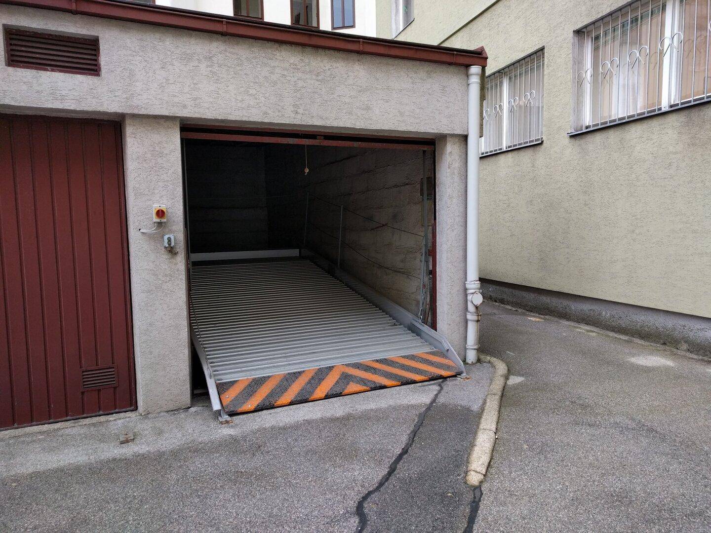 Eingang zu einer Tiefgarage mit automatischer Rampe und orange-schwarzen Warnstreifen.