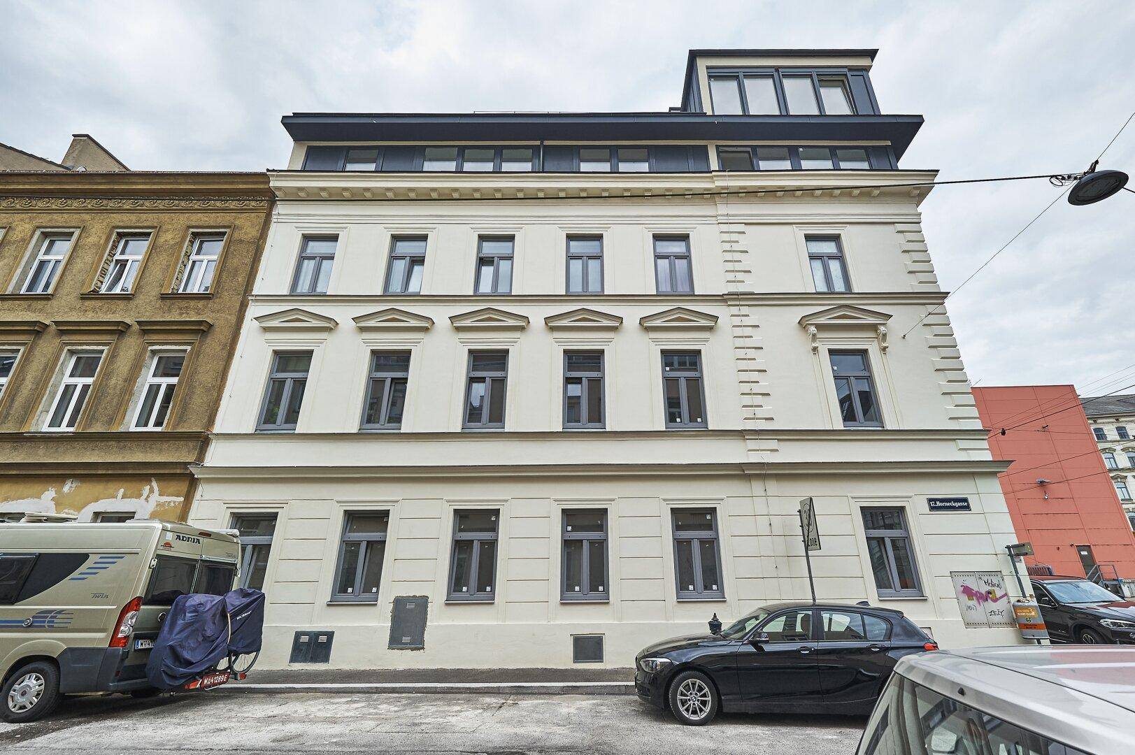 Historisches Gebäude mit moderner Dachaufstockung und großen Fenstern an einer Stadtstraße.