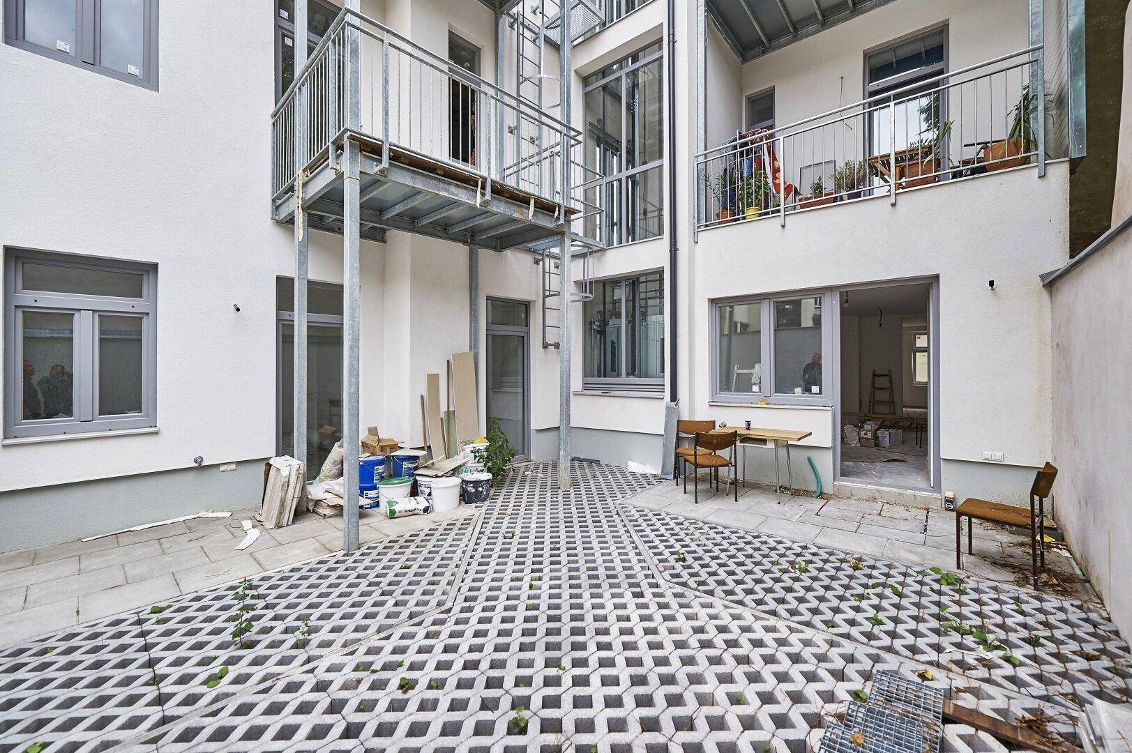 Innenhof mit Pflastersteinen und einem kleinen Sitzbereich, umgeben von Gebäudefassaden.