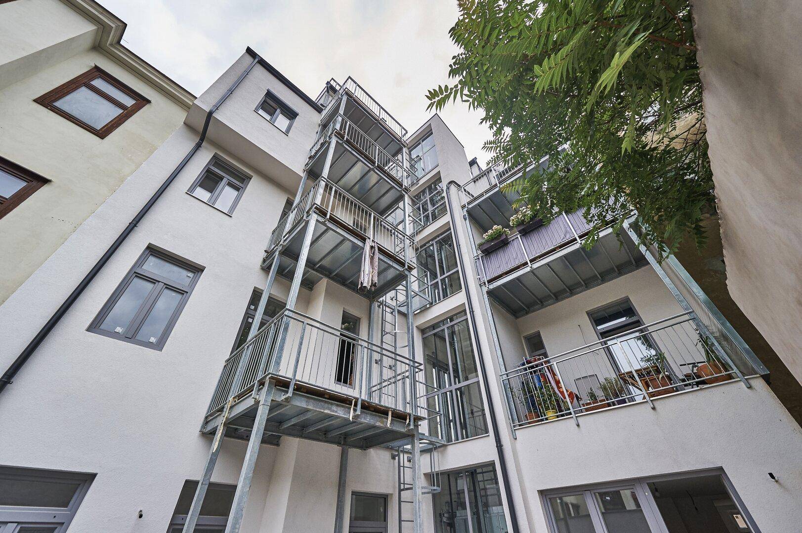 Moderne Gebäudefassade mit mehreren Balkonen und Außentreppen, die den Zugang zu den Wohnungen ermöglichen.