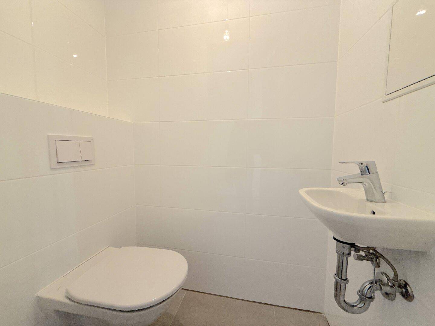 Modernes Gäste-WC mit wandhängender Toilette und kleinem Waschbecken, hell gefliest.