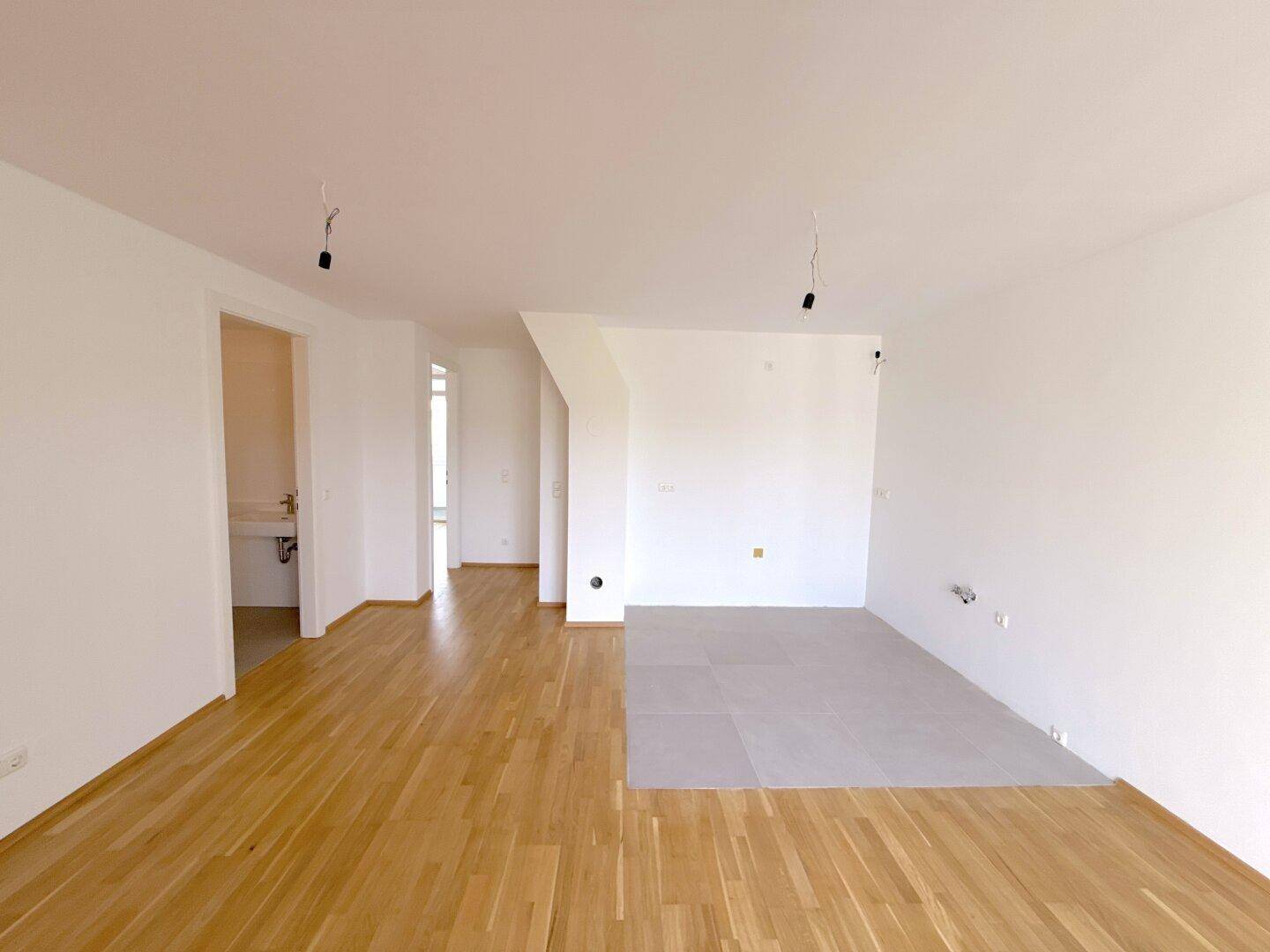 Geräumiger, heller Raum mit Parkettboden und einem gefliesten Bereich für eine offene Küche oder Essbereich.