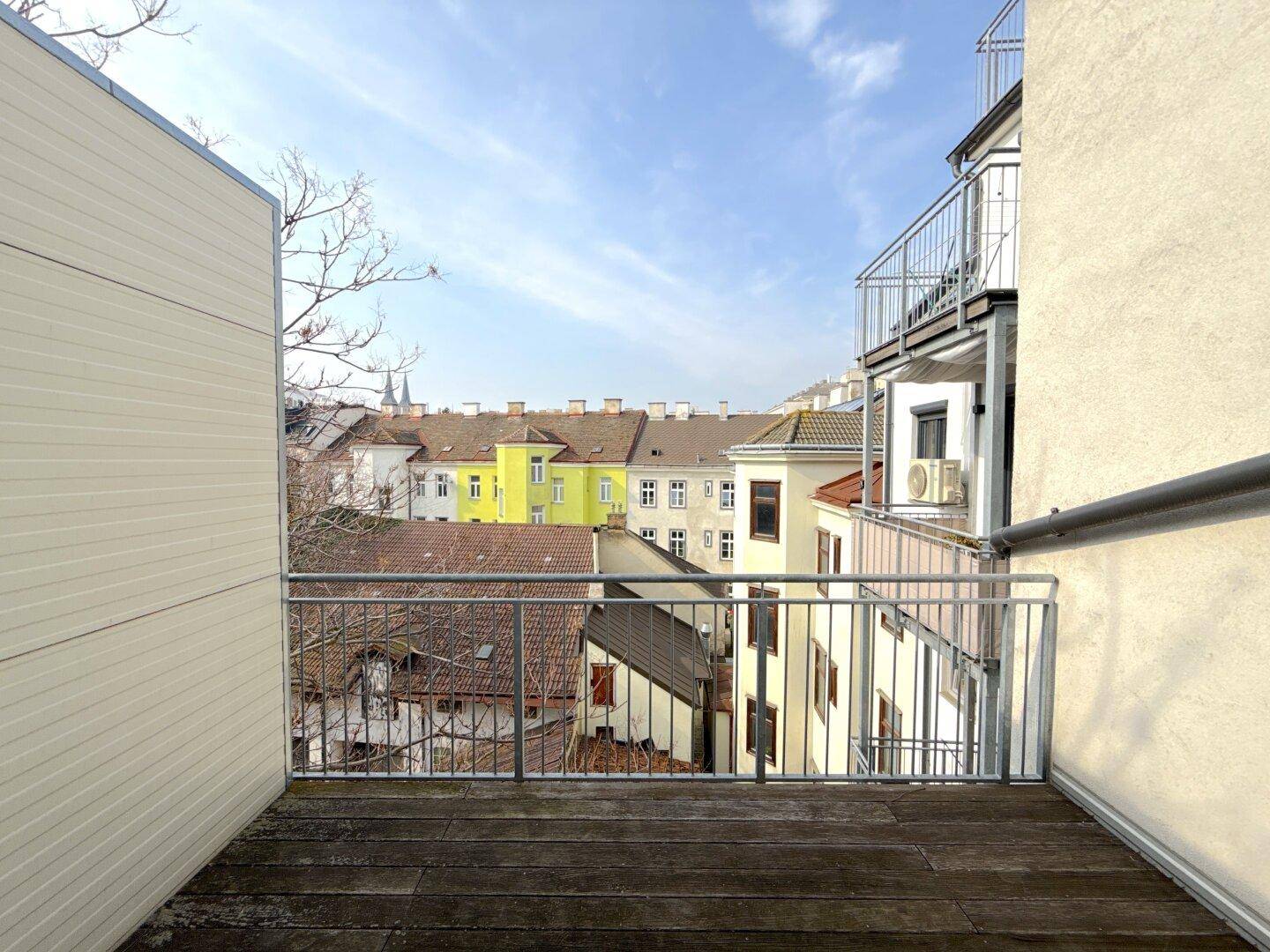 Balkon mit Holzboden und Metallgeländer, bietet einen weiten Blick über die Dächer der Stadt.