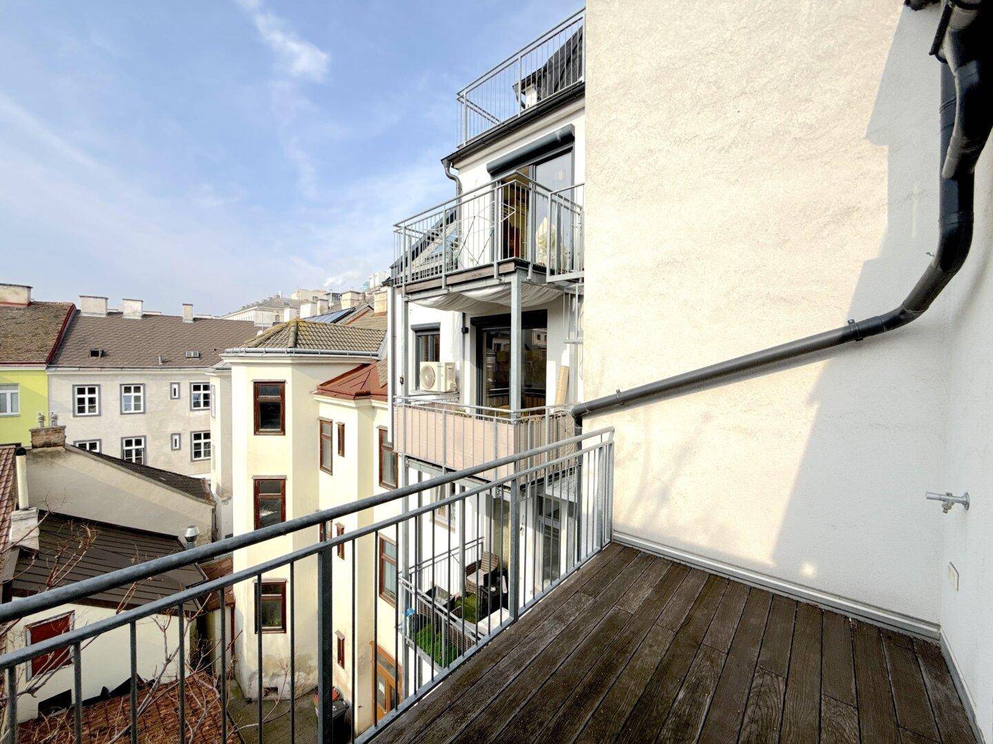 Balkon mit Holzboden und Metallgeländer, bietet einen weiten Blick über die Dächer der Stadt.