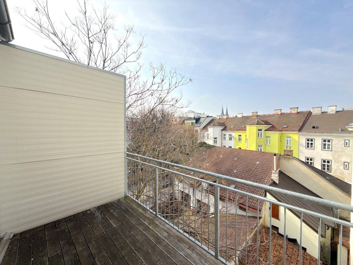 Balkon mit Holzboden und Metallgeländer, bietet einen weiten Blick über die Dächer der Stadt.
