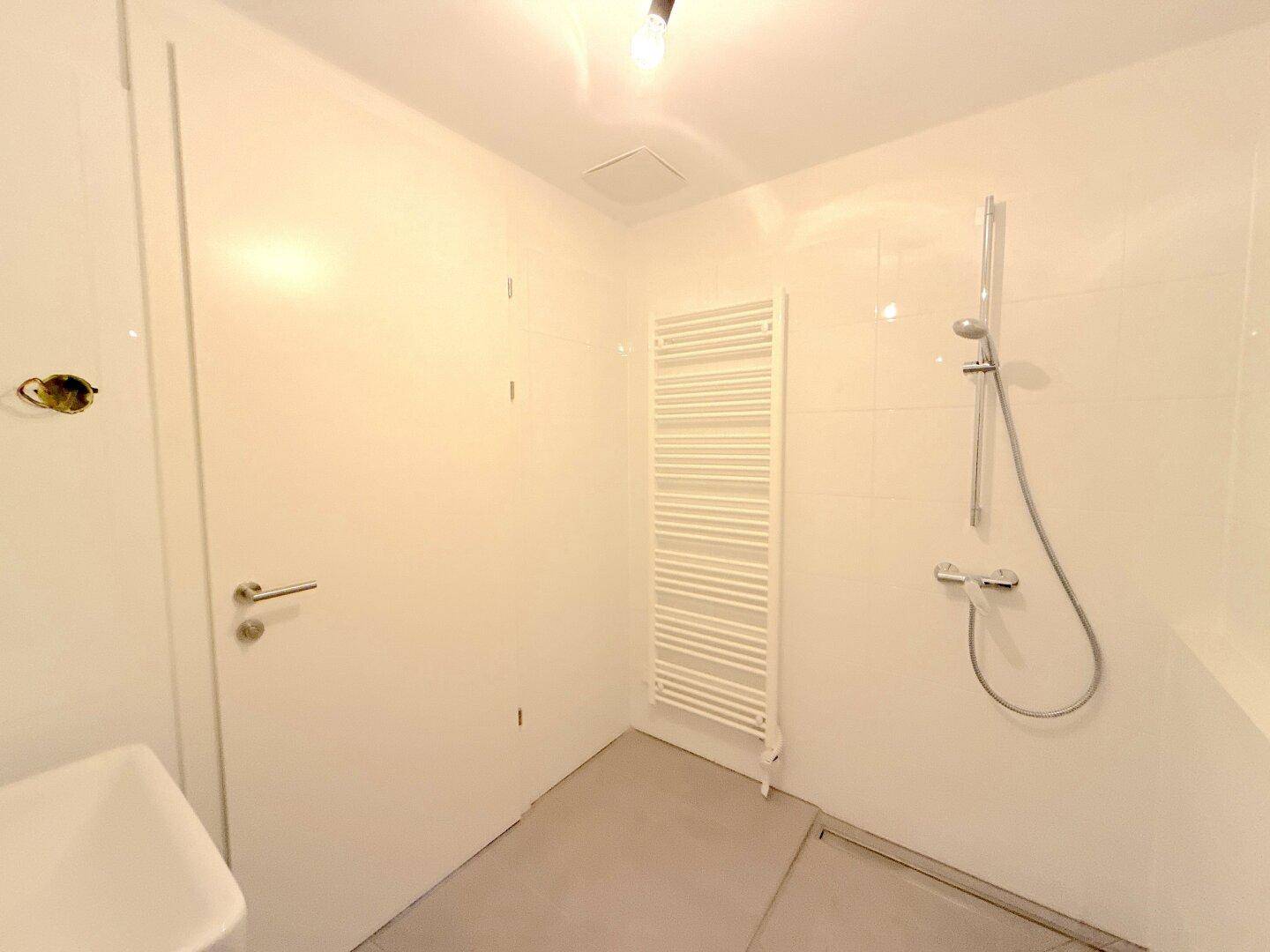 Modernes Badezimmer mit Dusche und beheiztem Handtuchhalter, hell gefliest und funktional.