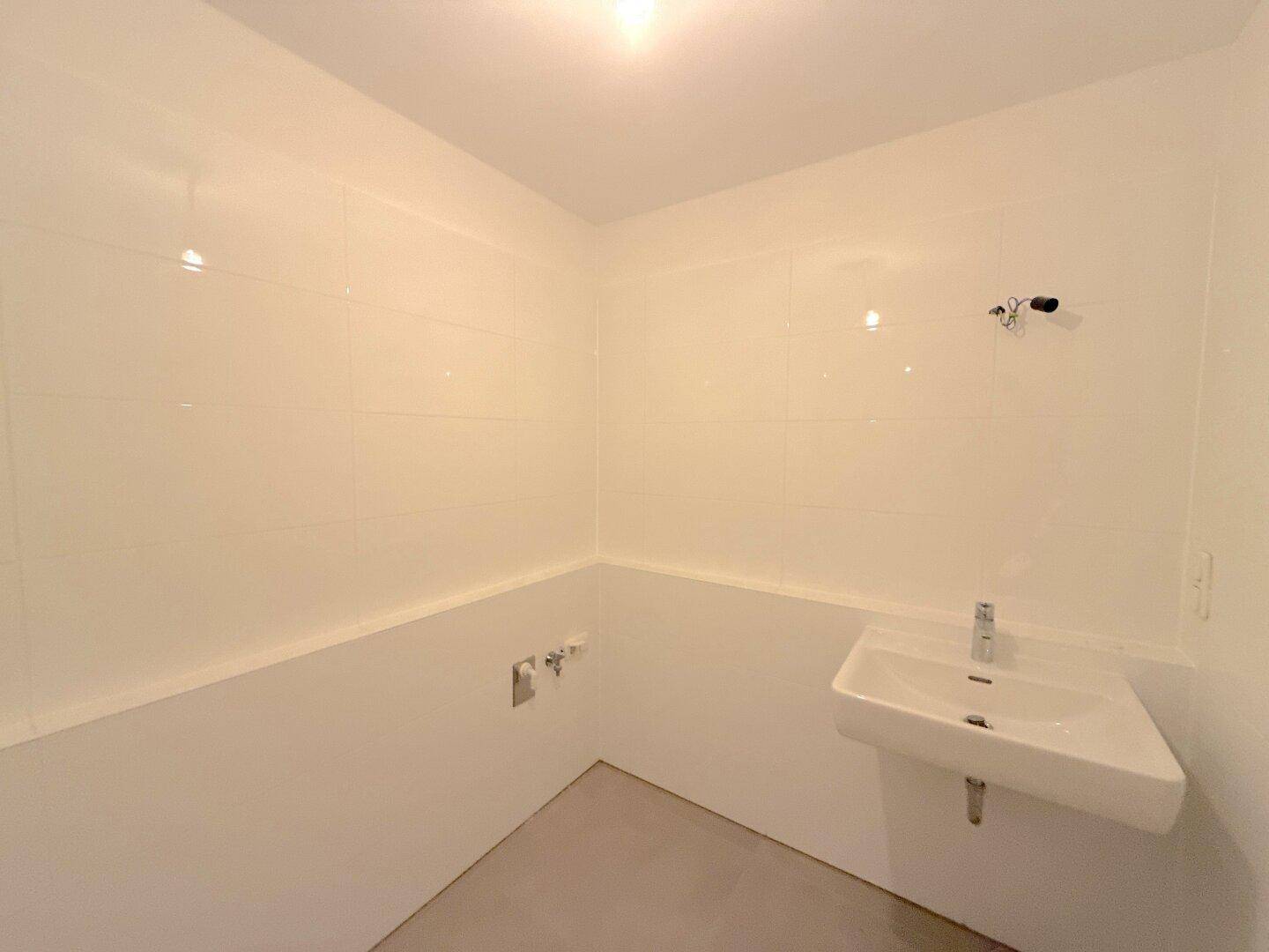 Modern gefliestes WC mit einem einzelnen Waschbecken und hellen Wänden, in neuwertigem Zustand.