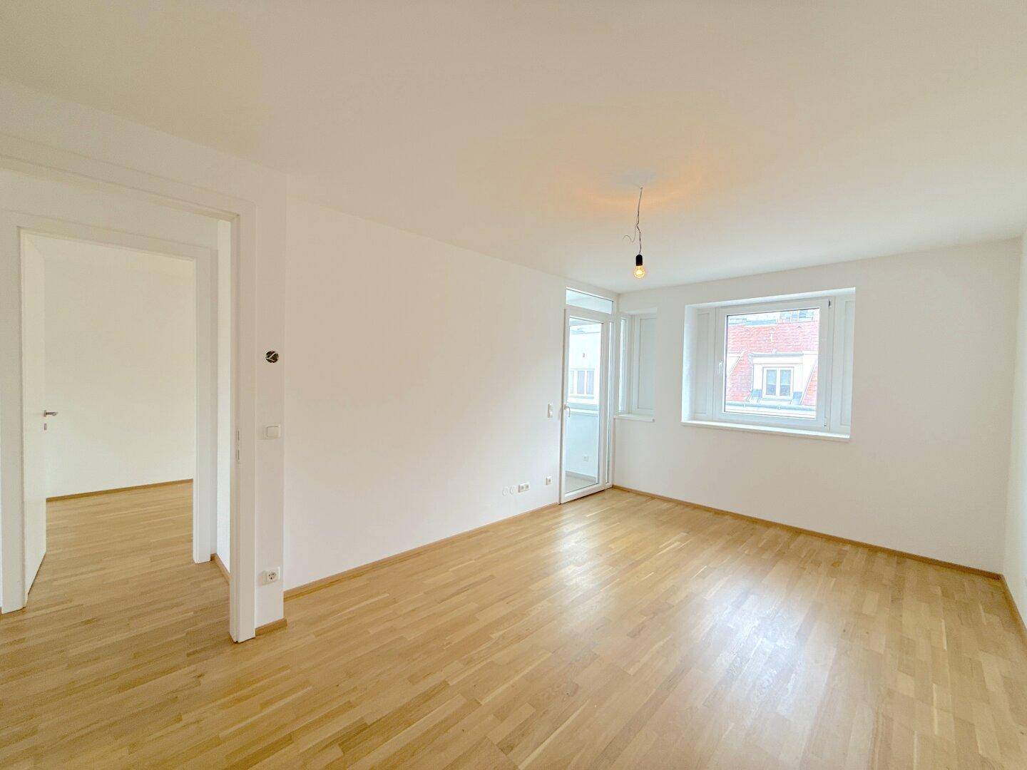 Heller Raum mit Parkettboden, einem Fenster und einer Balkontür, ideal für ein Schlaf- oder Wohnzimmer.