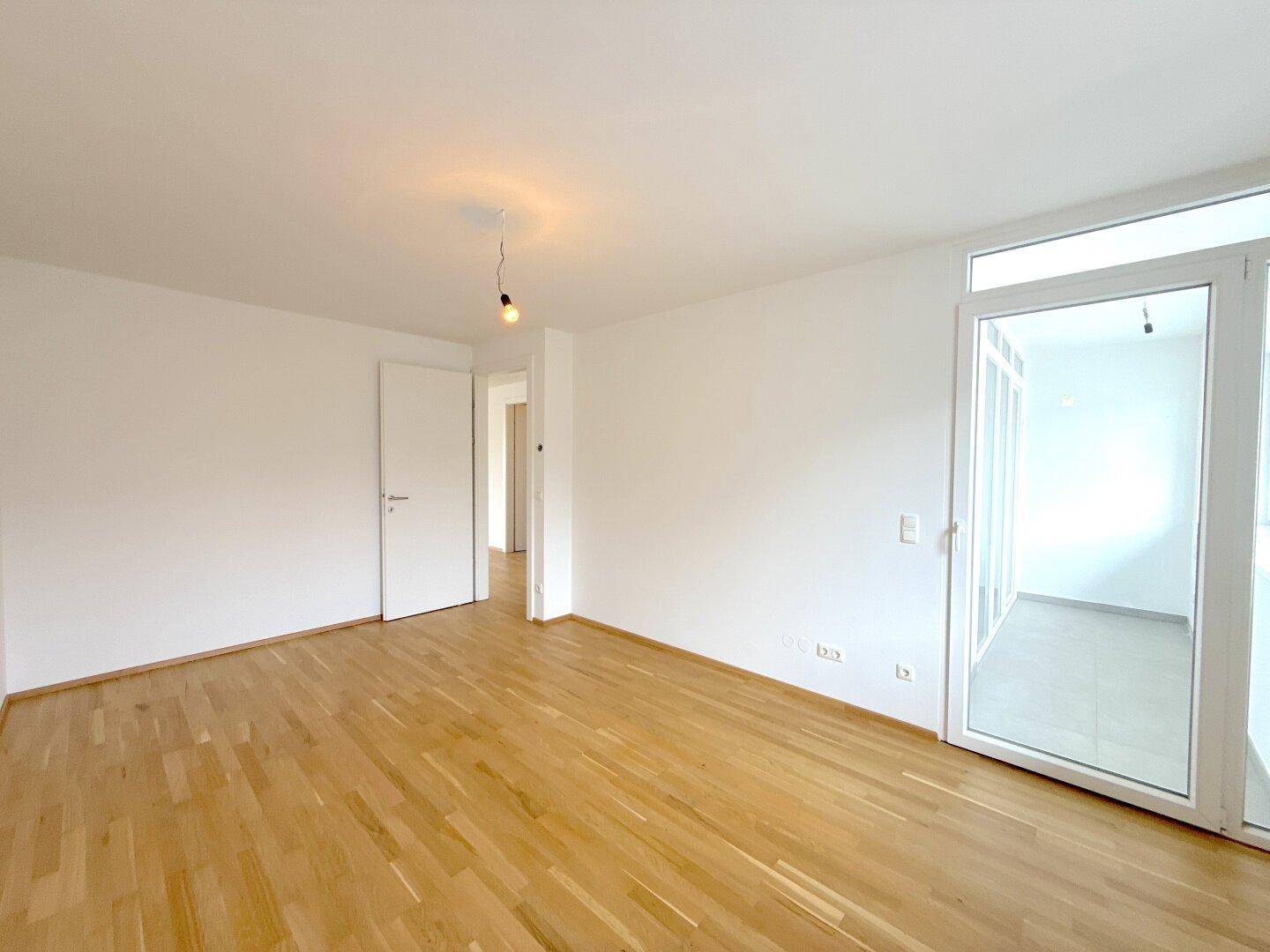 Heller Raum mit Parkettboden, einer Tür und Zugang zu einem weiteren Bereich oder Balkon.