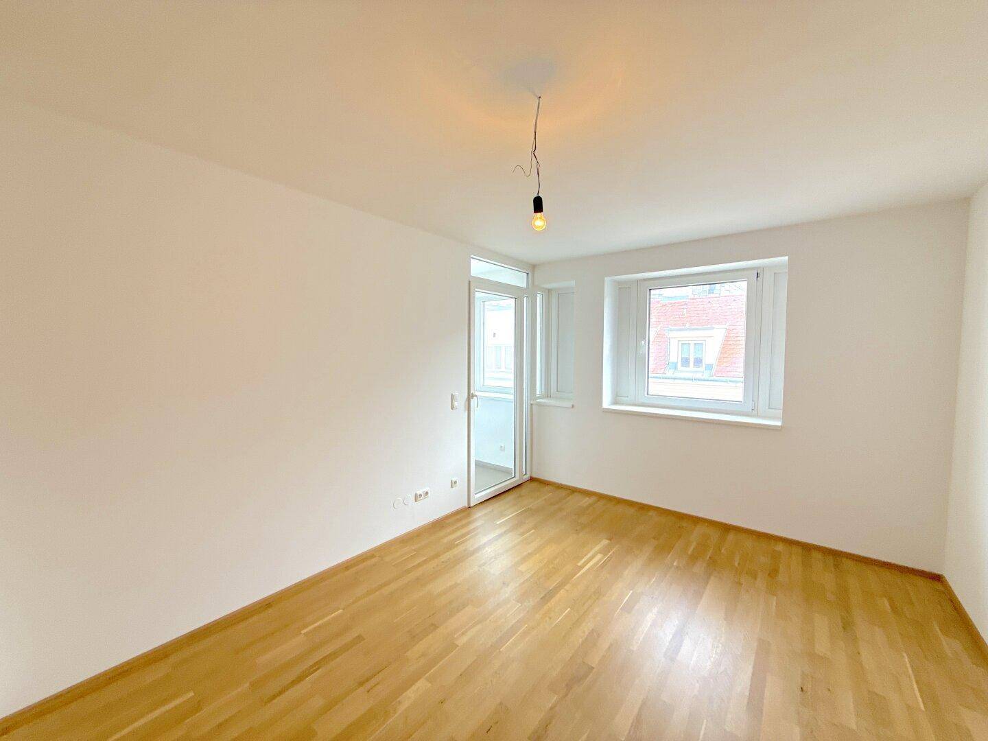 Lichtdurchfluteter Raum mit Parkettboden, einem Fenster und einer Balkontür, bietet viel Tageslicht.