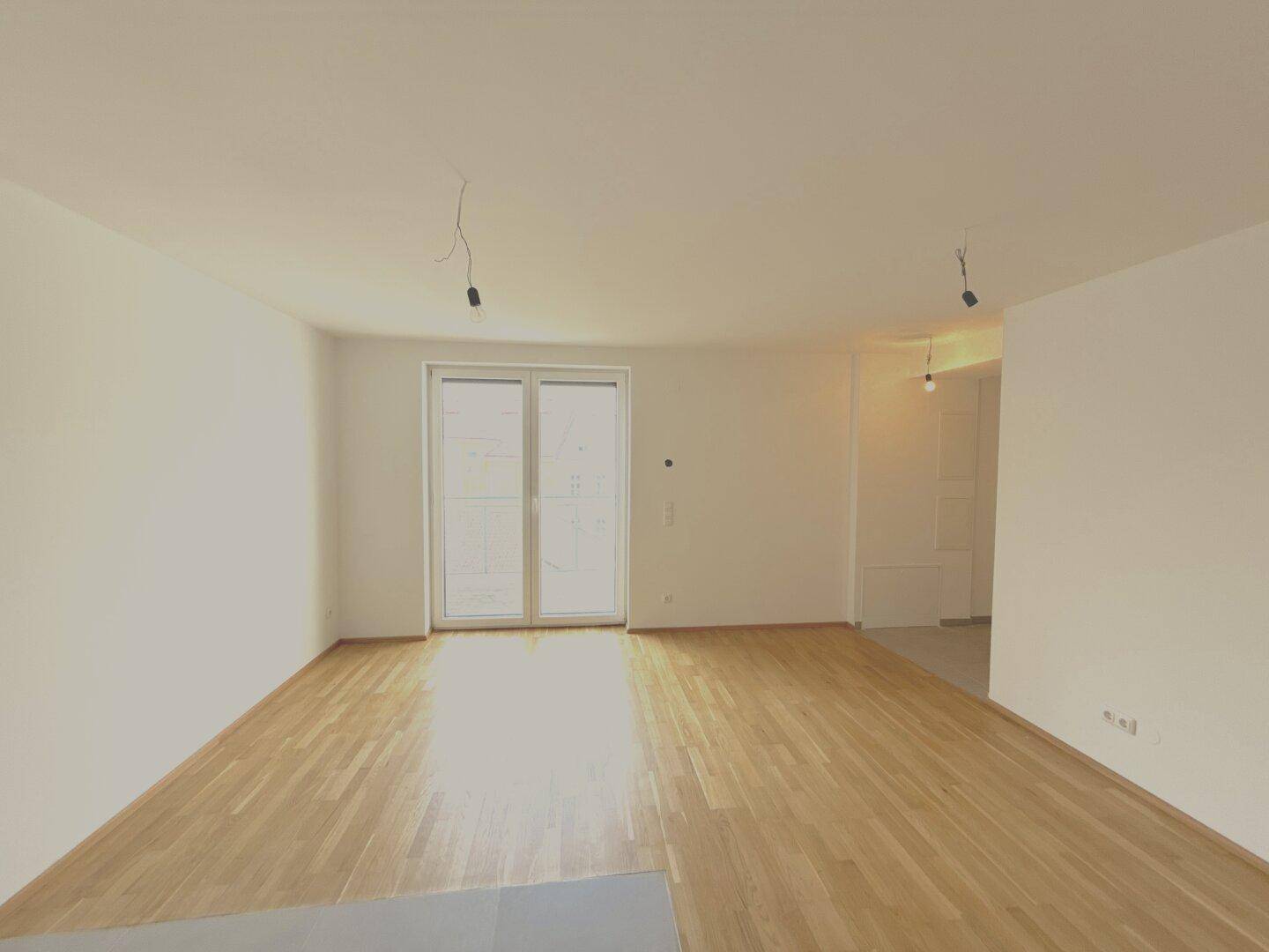 Geräumiger, heller Raum mit Parkettboden und einer großen Balkontür, die viel Licht hereinlässt.