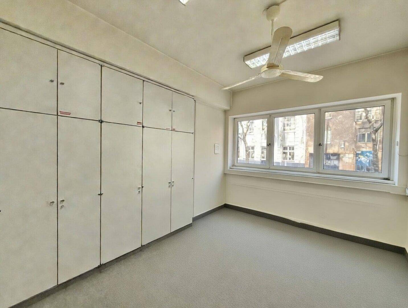 Funktionaler Büroraum mit Einbauschränken, Deckenventilator und Fenstern mit Blick nach draußen.