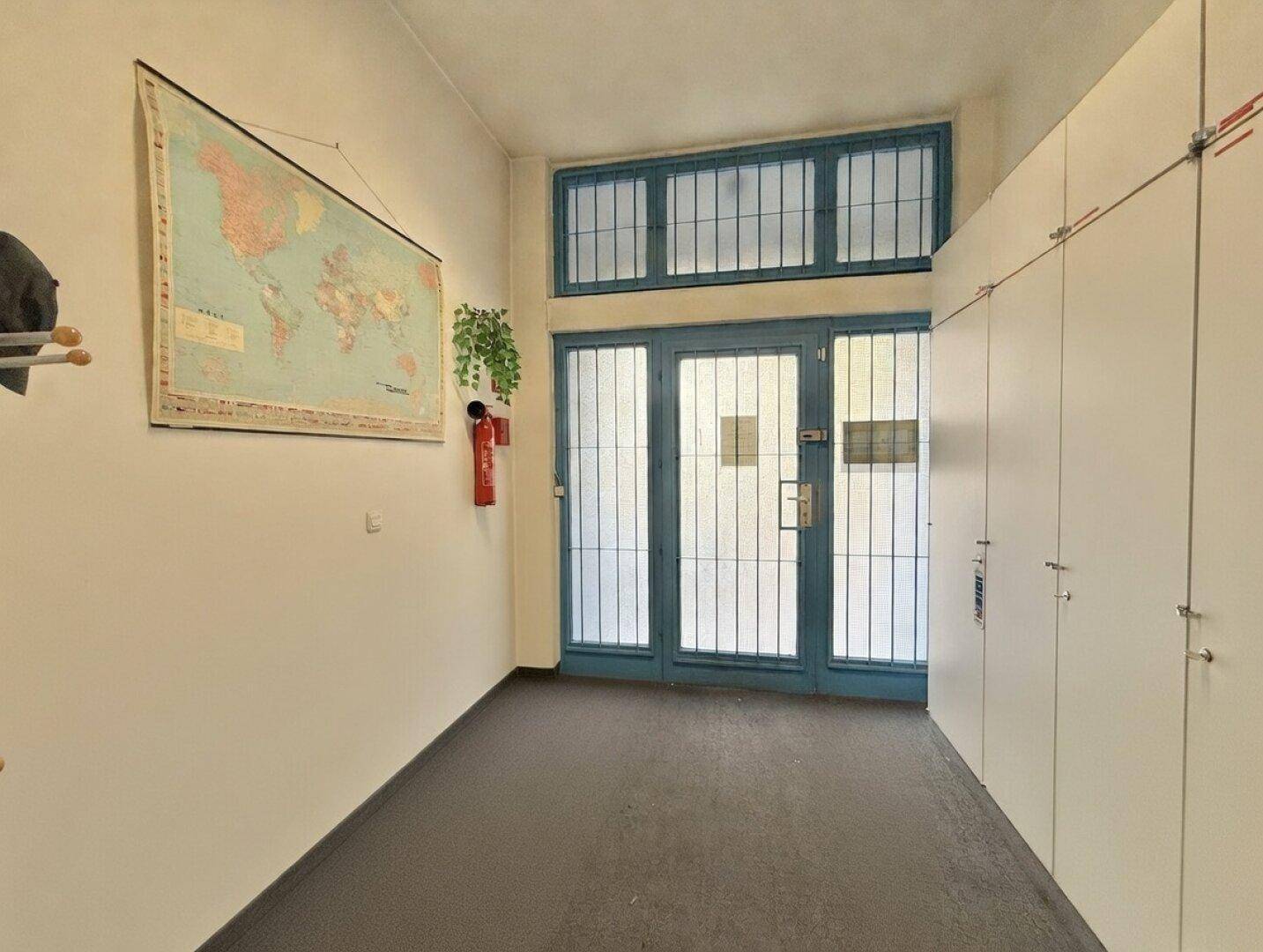 Eingangsbereich mit blauer Gittertür, weißen Spinden und einer Weltkarte an der Wand.