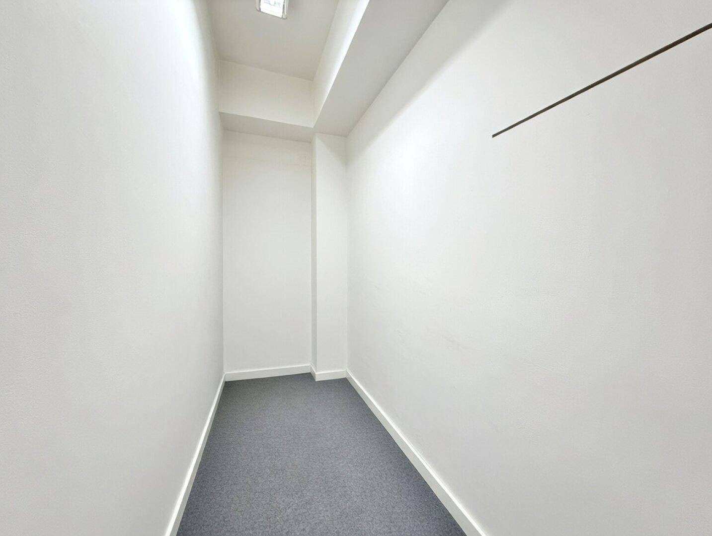 Kleiner, schmaler Raum mit weißen Wänden und grauem Teppichboden, ideal als Abstellkammer.