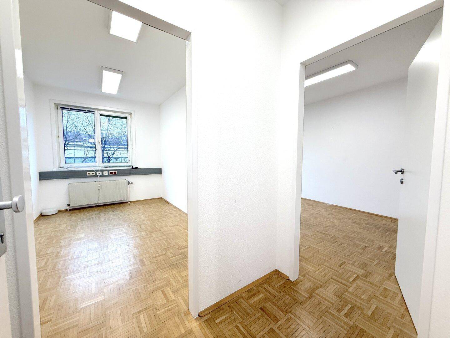 Heller Flur mit Zugang zu zwei leeren Büroräumen, alle mit Parkettboden und weißen Wänden.