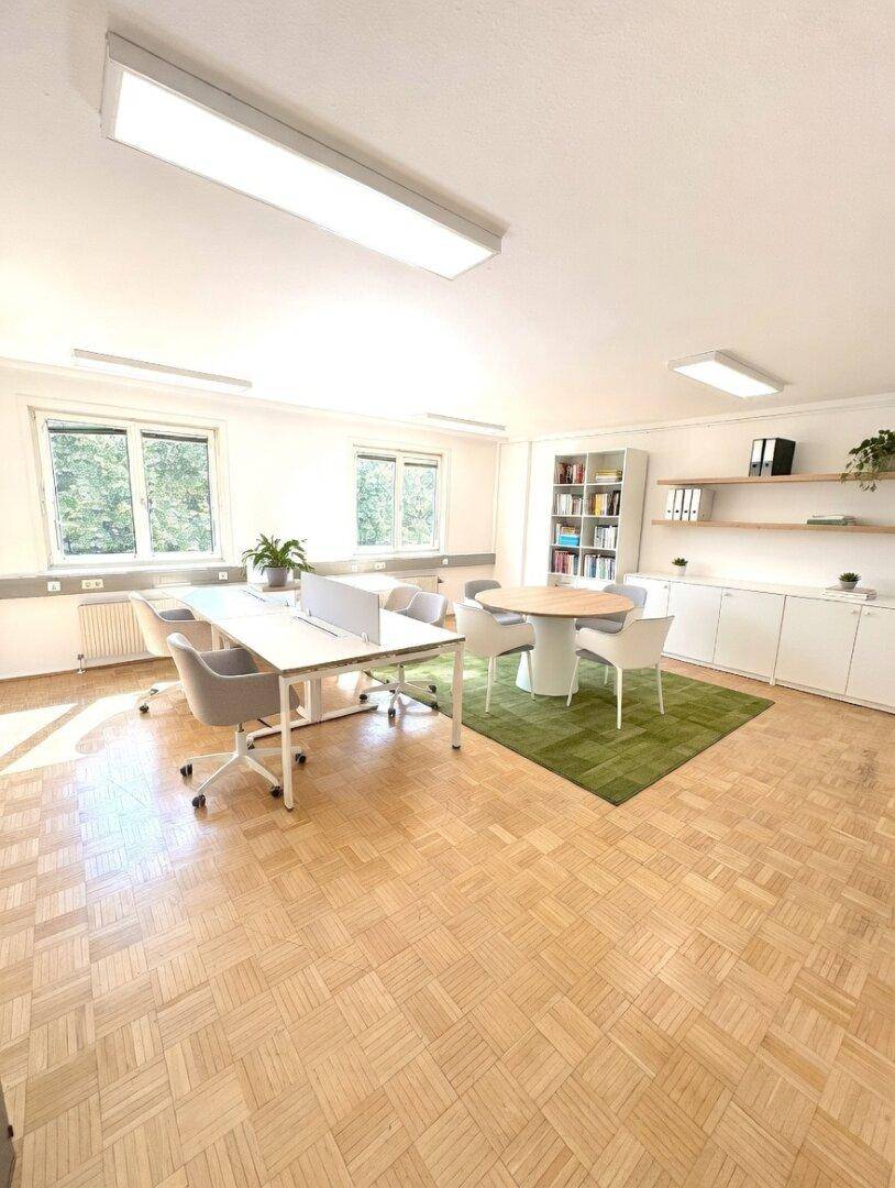 Großes Büro mit mehreren Arbeitsplätzen, einem runden Besprechungstisch und Blick ins Grüne.