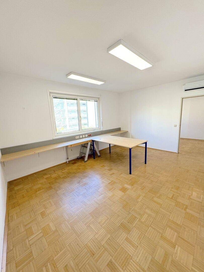 Büroraum mit Parkettboden, einem Tisch, einer Ablagefläche und Klimaanlage an der Wand.