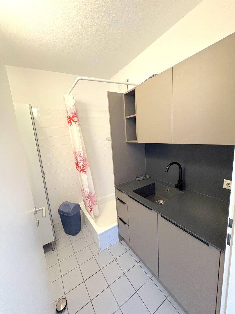 Kleines Badezimmer mit Badewanne, Duschvorhang und einem Waschbecken mit Unterschrank.