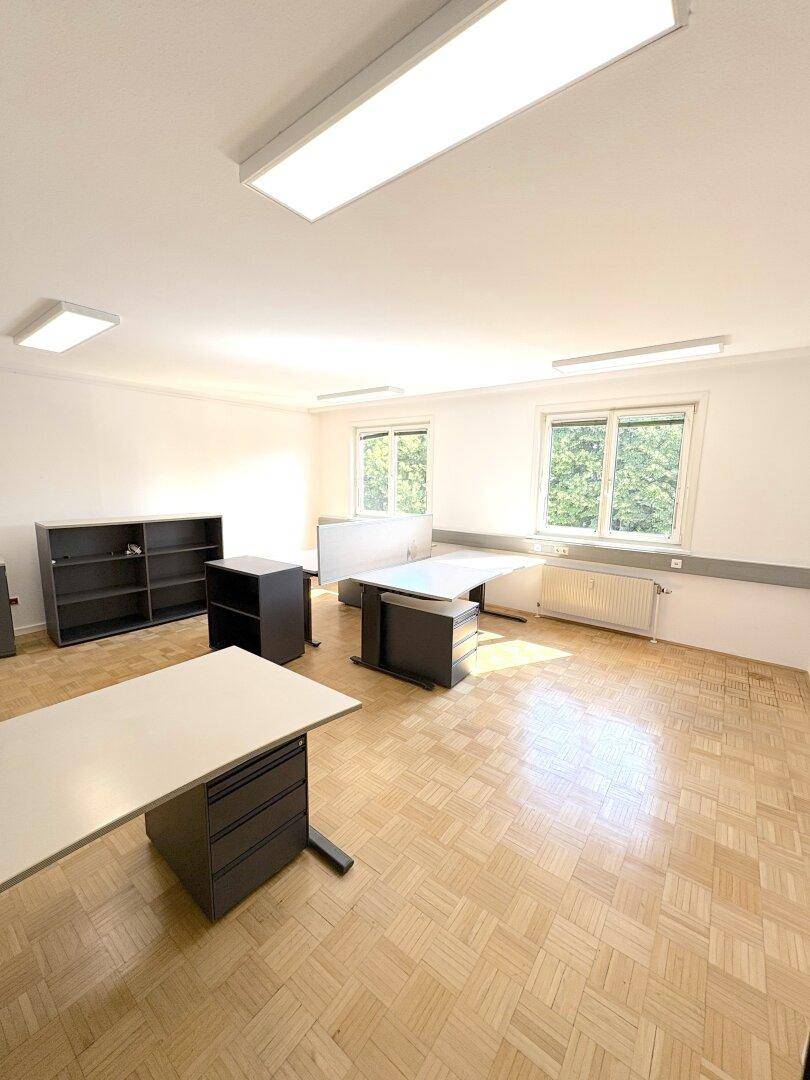 Büroraum mit Parkettboden, mehreren Fenstern und dunklen Büromöbeln.
