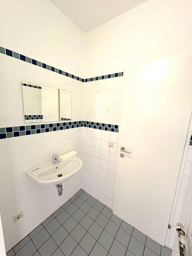 Badezimmer mit weiß gefliesten Wänden, blau-grünen Akzentfliesen und einem Waschbecken.