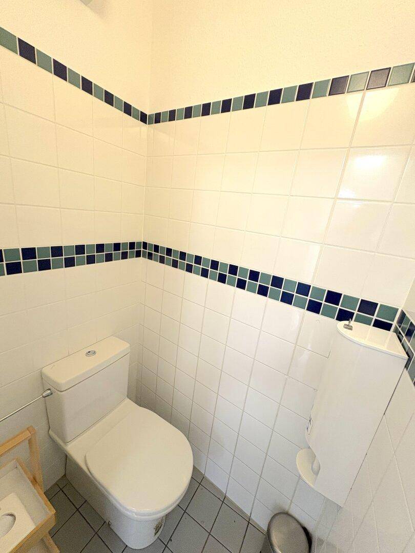 Separate Toilette mit weiß gefliesten Wänden, blau-grünen Akzentfliesen und einer Toilette.