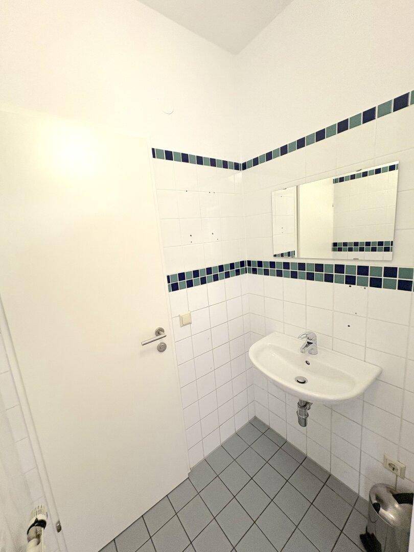 Badezimmer mit weiß gefliesten Wänden, blau-grünen Akzentfliesen und einem Waschbecken.