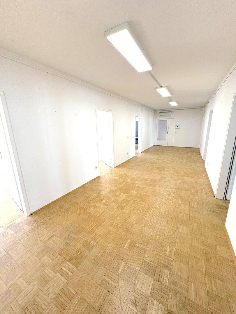 Geräumiger, leerer Büroraum mit hellem Parkettboden und mehreren Türen.