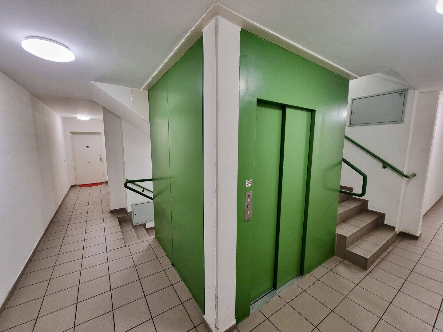 Gemeinschaftlicher Flur mit Aufzug und Treppenhaus, gut beleuchtet und funktional.