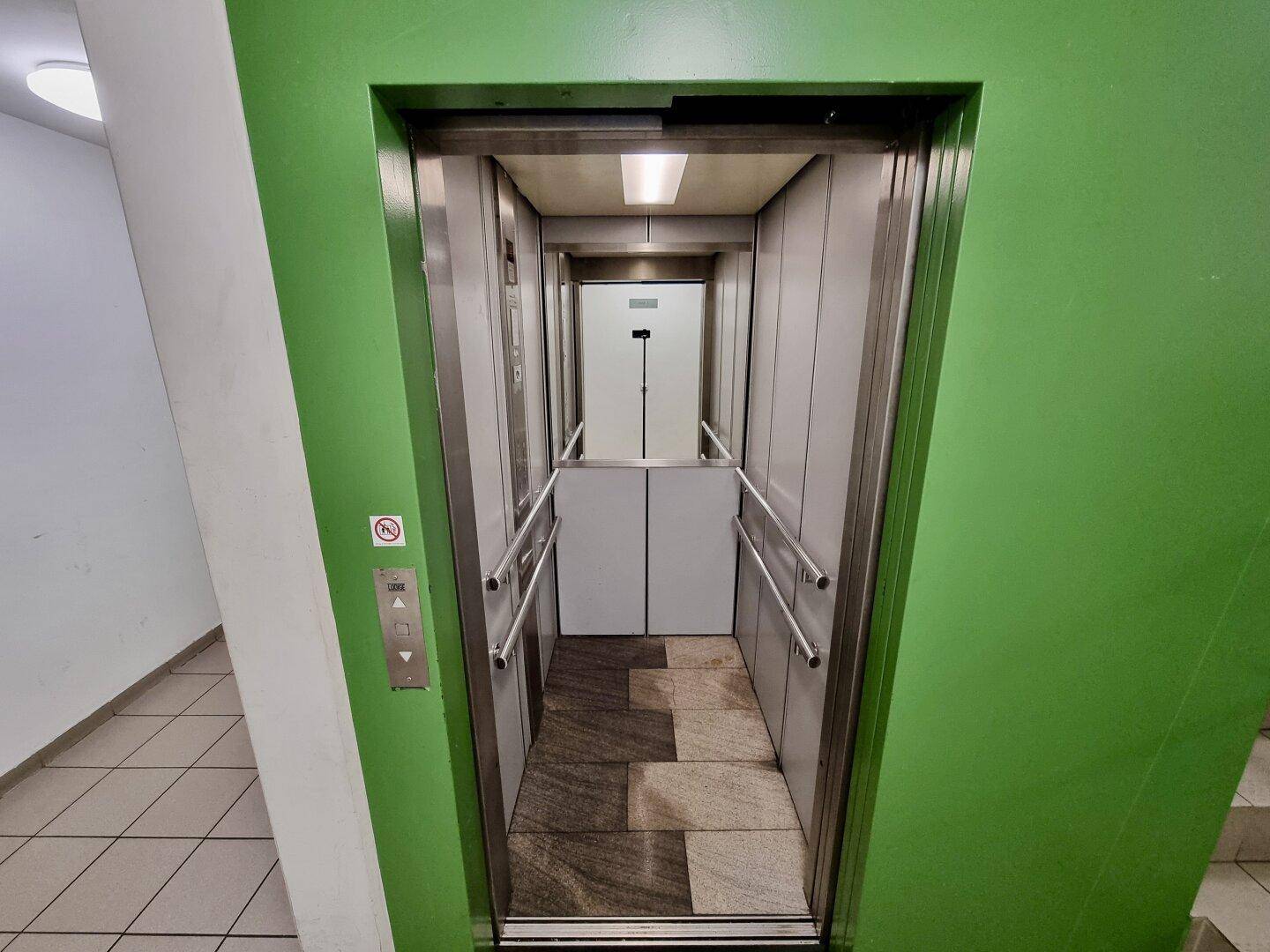 Innenansicht des Aufzugs mit Metallwänden und gemustertem Boden, bereit zur Fahrt.