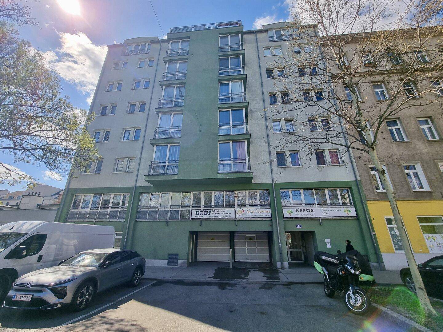 Mehrstöckiges Wohngebäude mit grüner Fassade und vielen Fenstern an einer Stadtstraße.
