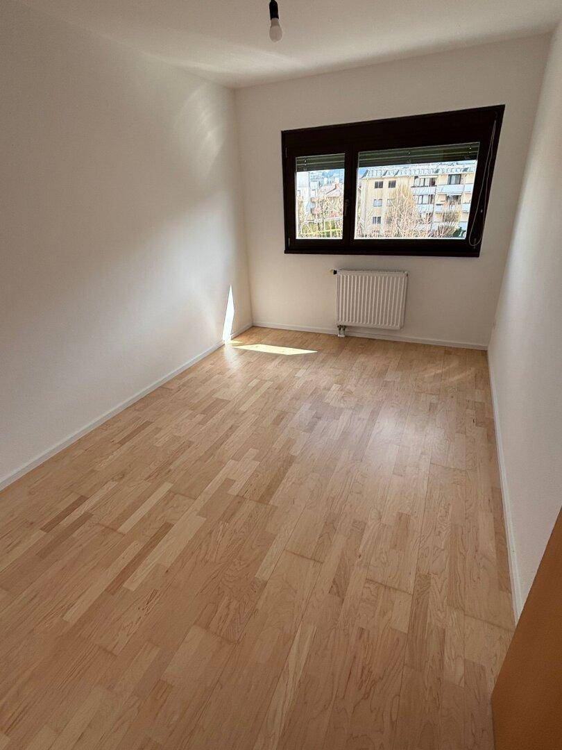 Helles Schlafzimmer mit Parkettboden und Fenster, das viel Tageslicht in den Raum lässt.