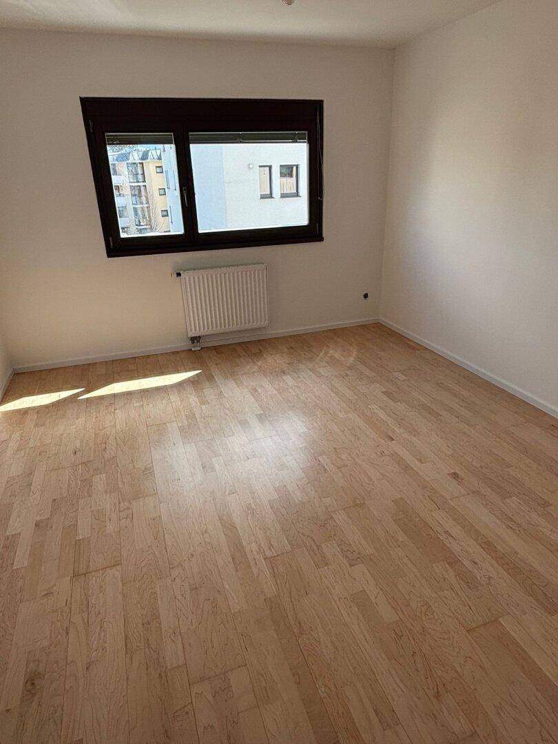 Geräumiges Schlafzimmer mit hellem Parkettboden und großem Fenster, bietet eine ruhige Atmosphäre.