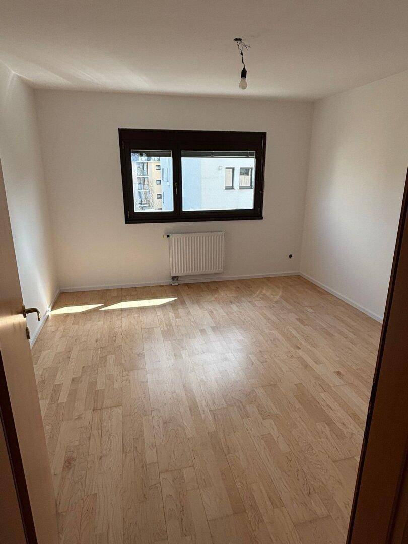 Lichtdurchflutetes Schlafzimmer mit Parkettboden und Blick nach draußen, ideal für erholsame Nächte.