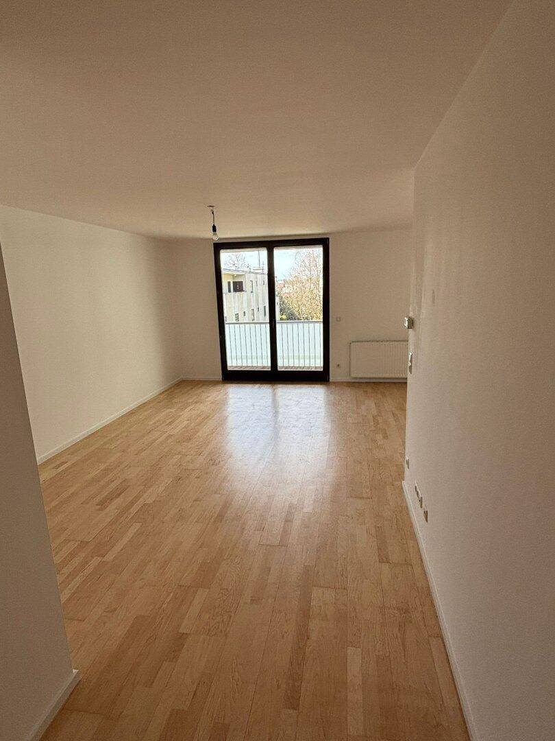Lichtdurchfluteter Wohnbereich mit hellem Parkett und Zugang zum Balkon, ideal für offene Gestaltung.
