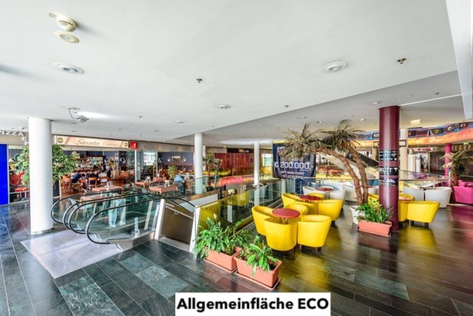 Helle Ladenpassage mit Rolltreppen, Sitzgelegenheiten und Geschäften im Hintergrund.